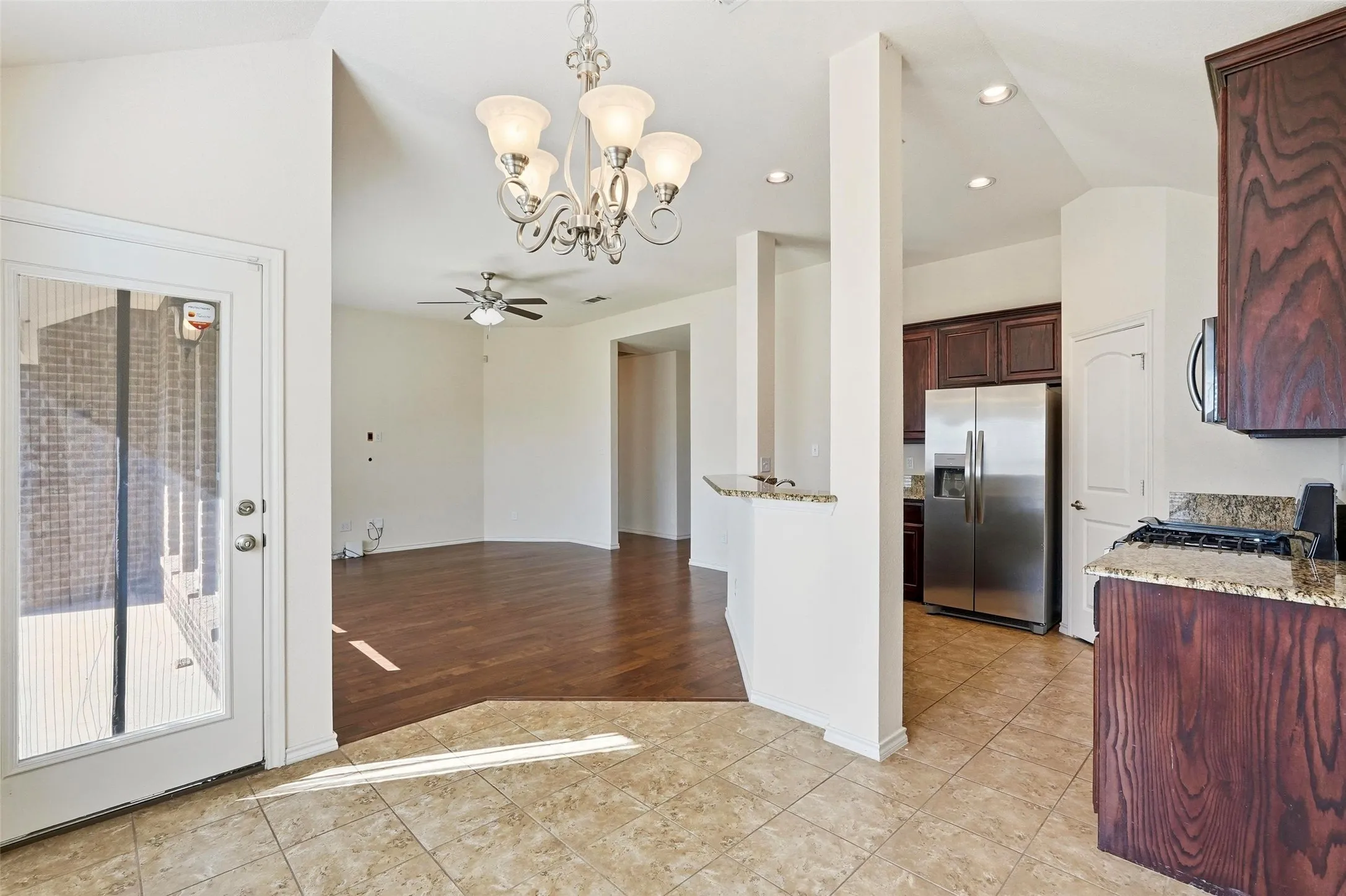 Tiled flooring in kitchen area with dark wood-finish cabinetry, stainless steel refrigerator, and granite countertops