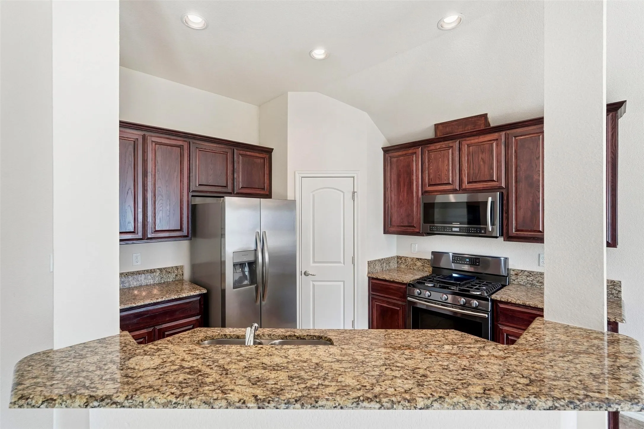 Kitchen featuring granite countertops, dark wood cabinetry, stainless steel appliances, and a built-in kitchen sink