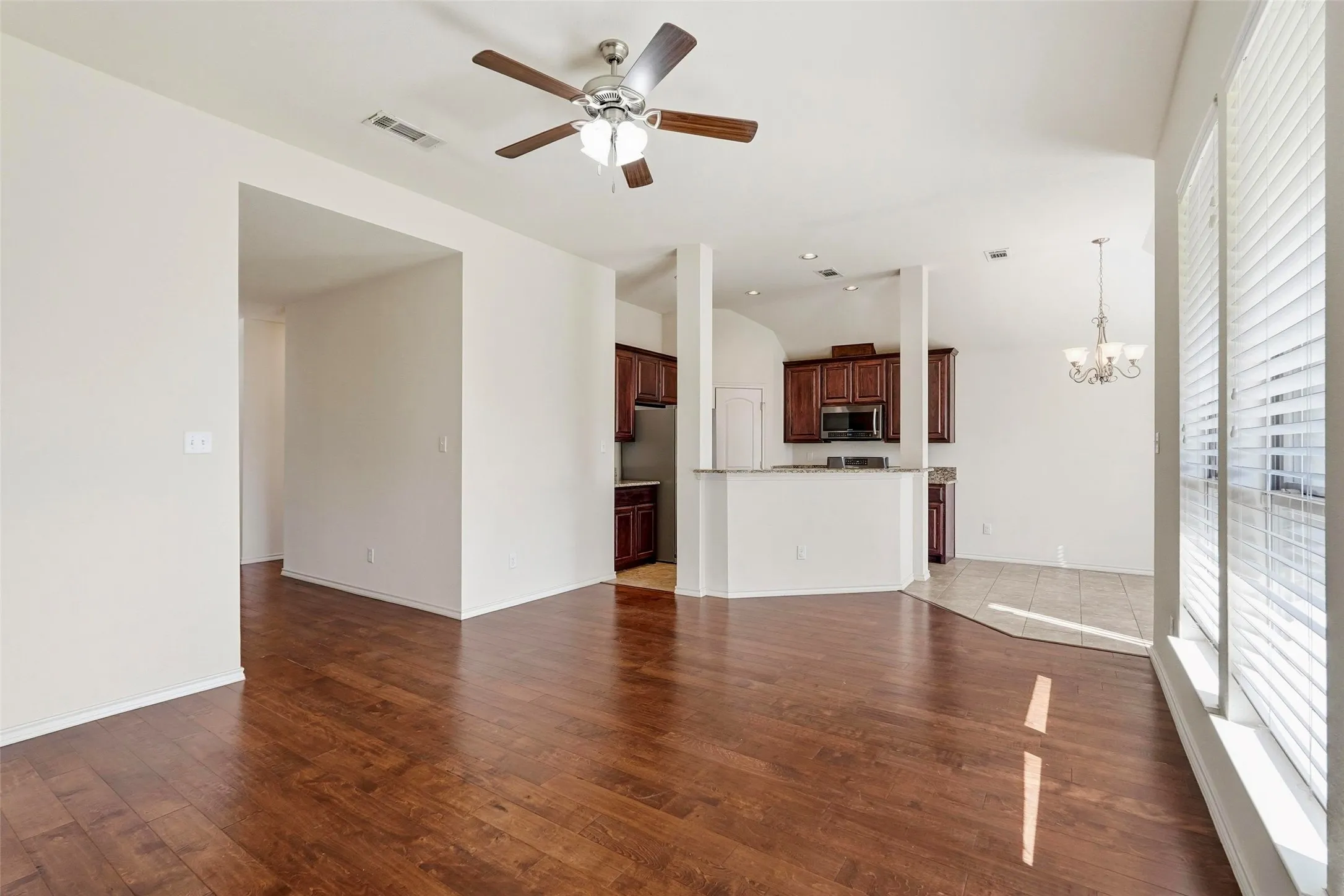 Wood-finish flooring, recessed lighting, ceiling fan, dark wood cabinetry, and a kitchen peninsula with a stone-look countertop
