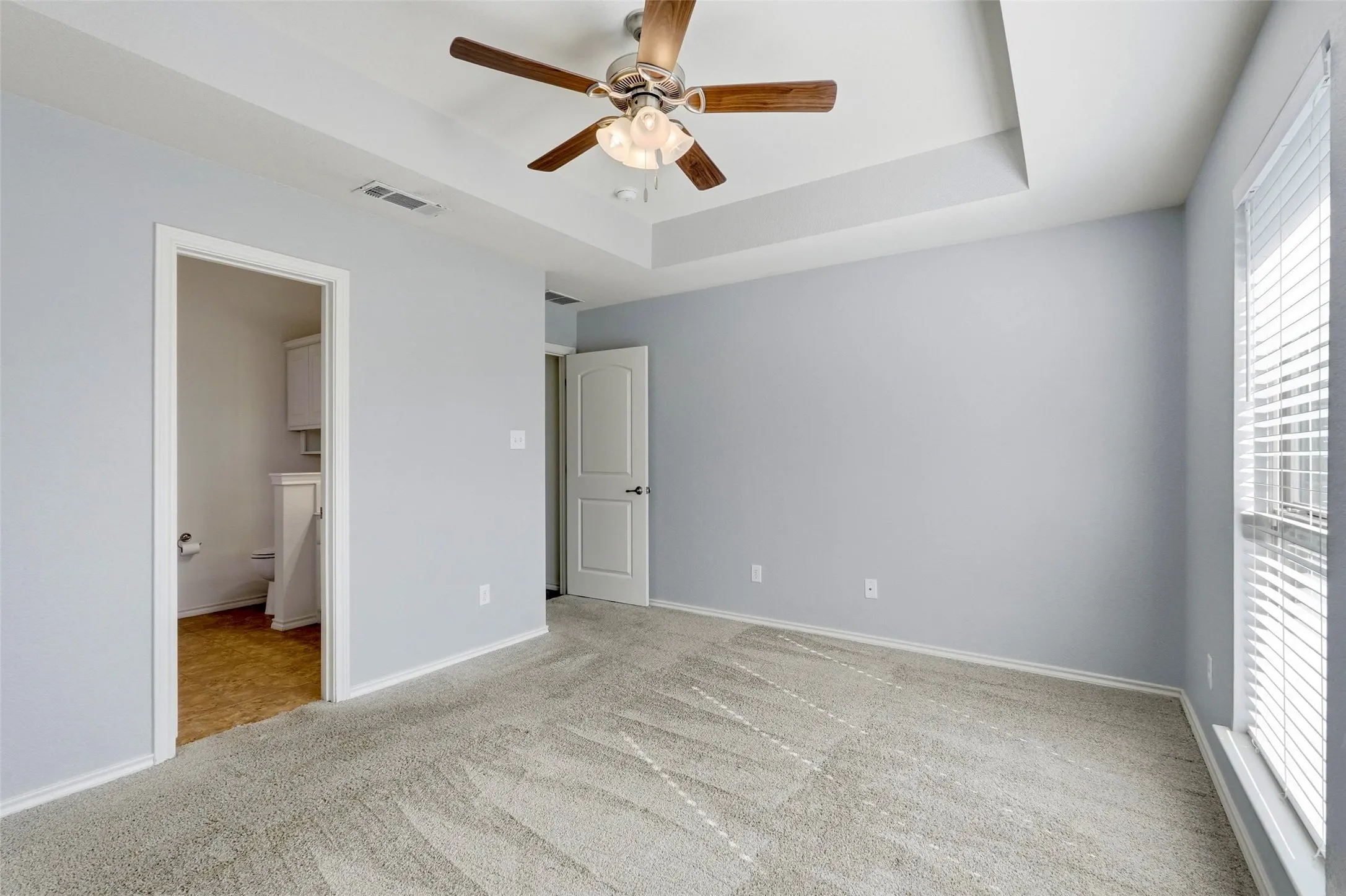 Recessed ceiling with an integrated ceiling fan, light gray wall finishes, and a large window with blinds
