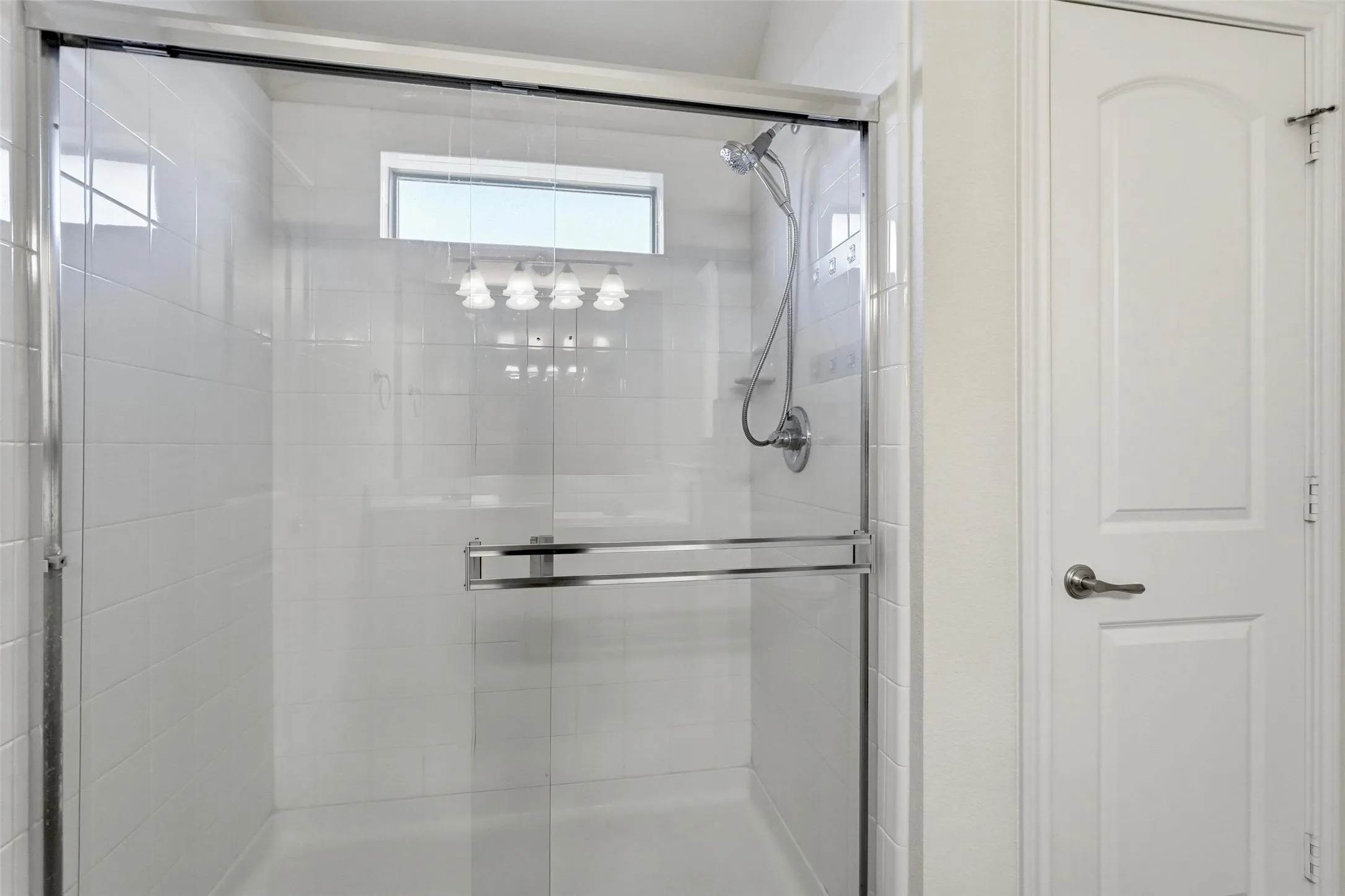 Enclosed shower with clear glass sliding door, polished chrome fixtures, white subway tile surround, and an integrated transom window