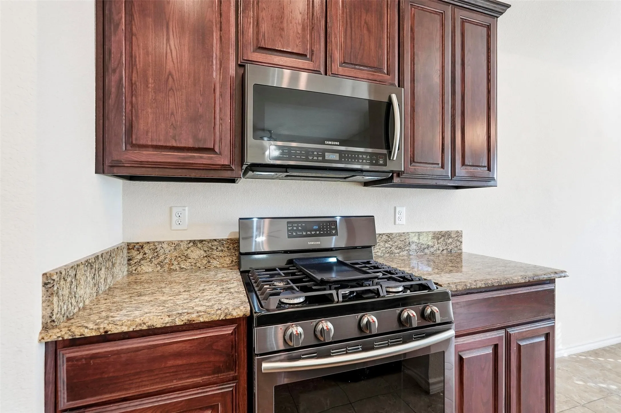 Stainless steel oven with a gas cooktop, granite-finish countertops, wood-finish cabinetry, and an integrated microwave
