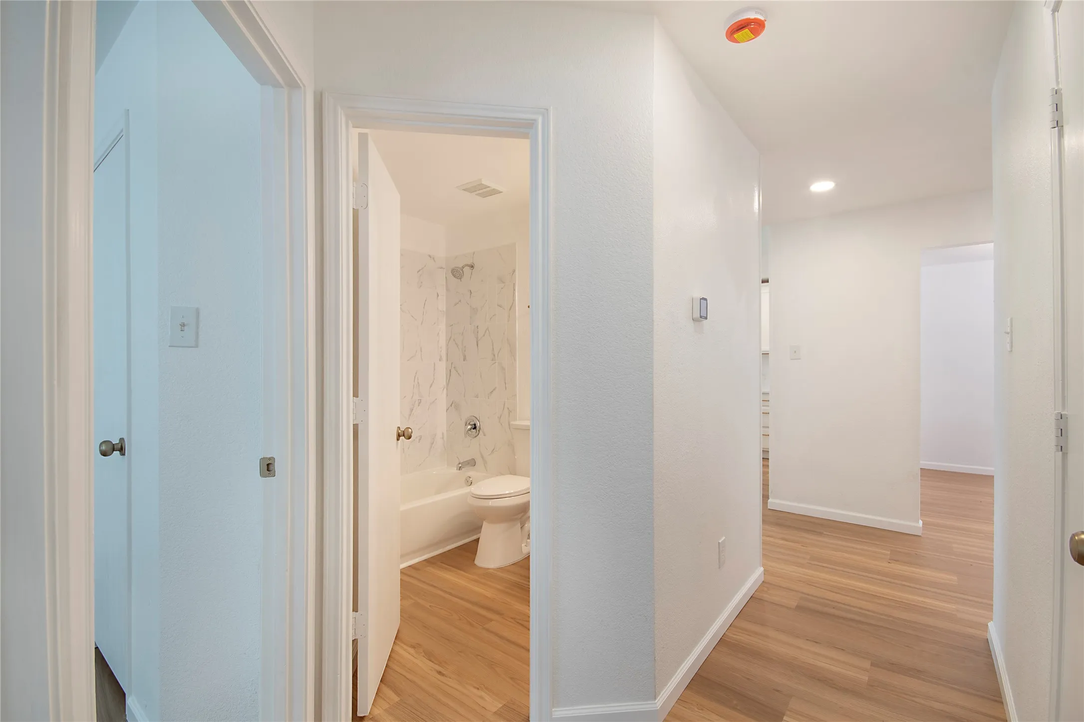 Wood-finish flooring throughout, white interior doors, and a bathroom featuring a tub with a tiled surround
