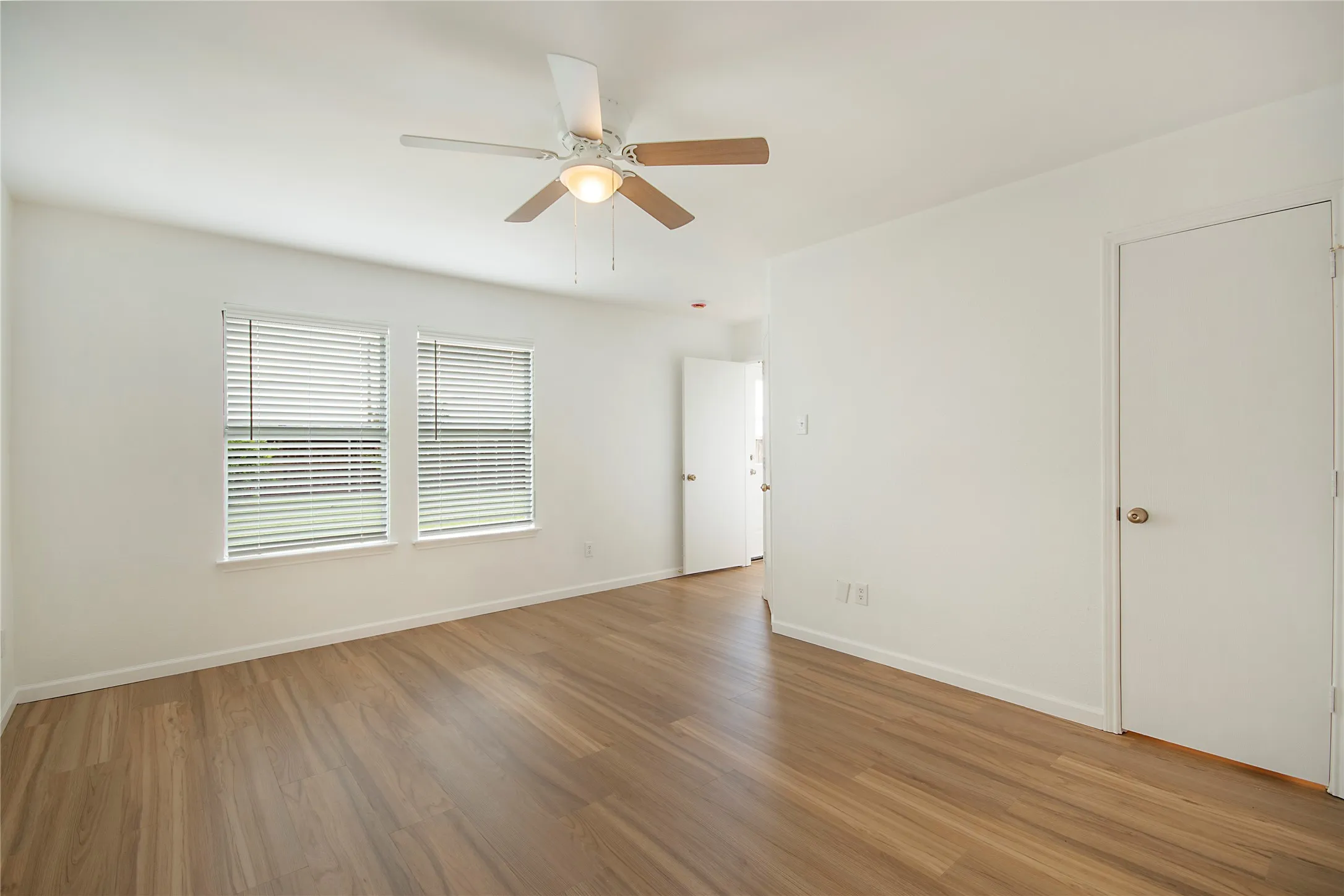 Wood-finish flooring throughout, two windows with blinds, and a ceiling fan with light fixture