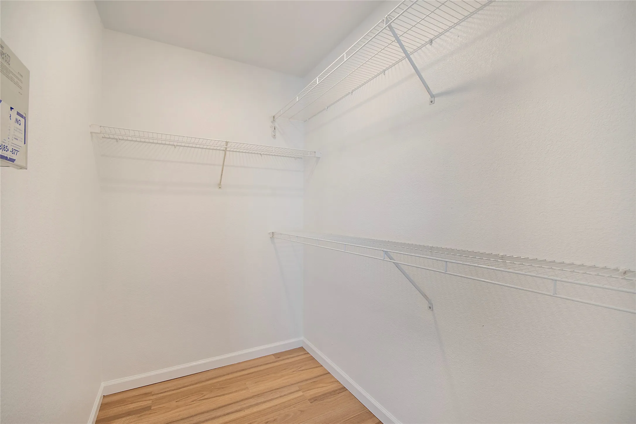 Wood-finish flooring with white baseboards, textured white walls, and multiple white wire shelving units
