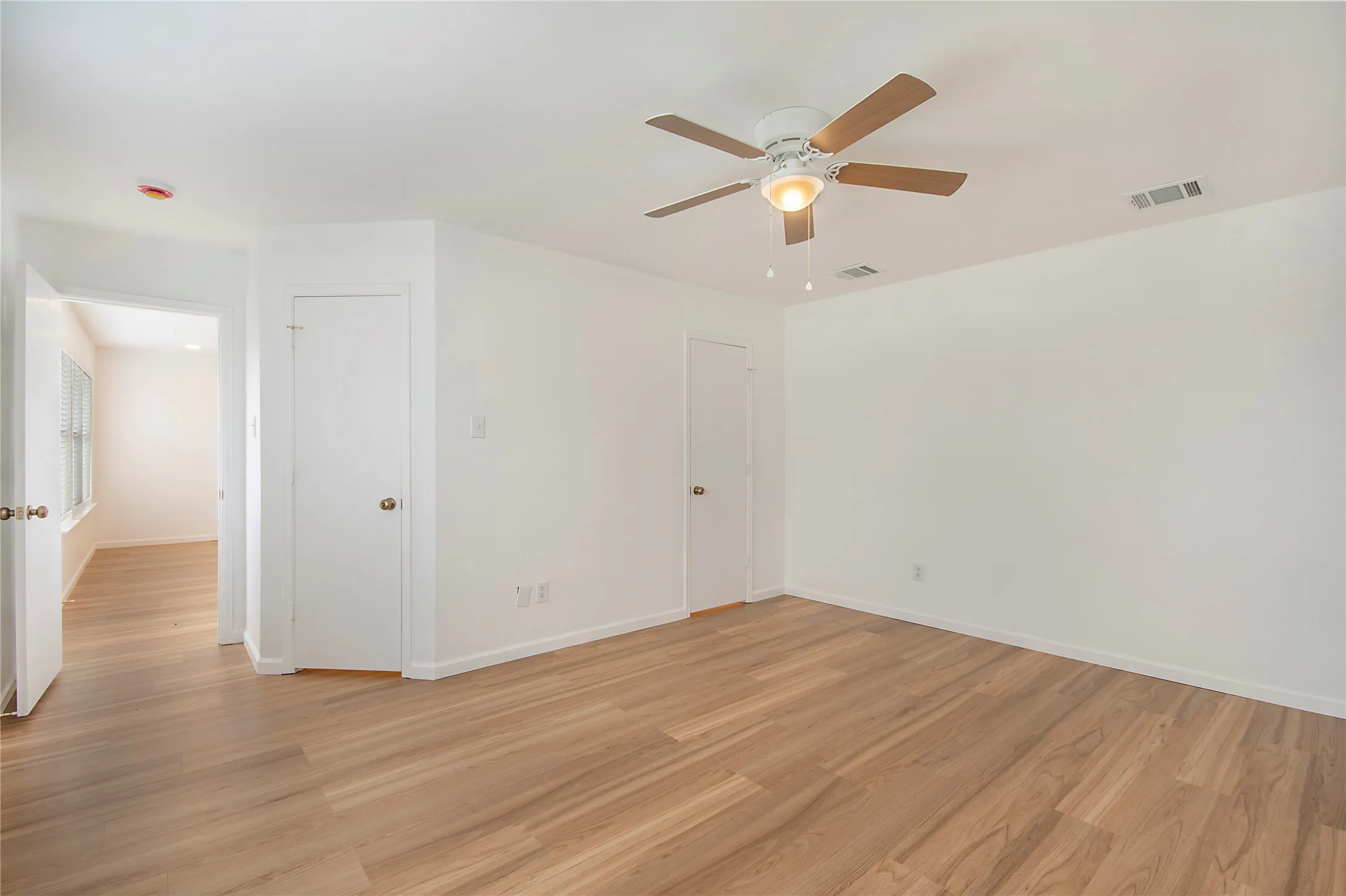Wood-finish flooring throughout, bright white walls, and a ceiling fan with integrated lighting