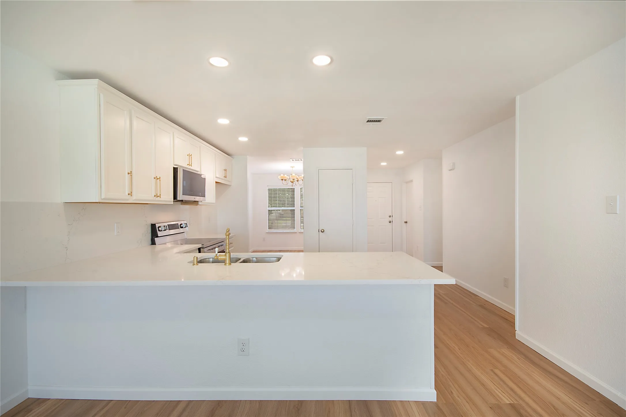Kitchen featuring white cabinetry with gold-toned hardware, stainless steel appliances, a brass-finish faucet, and light-toned countertops