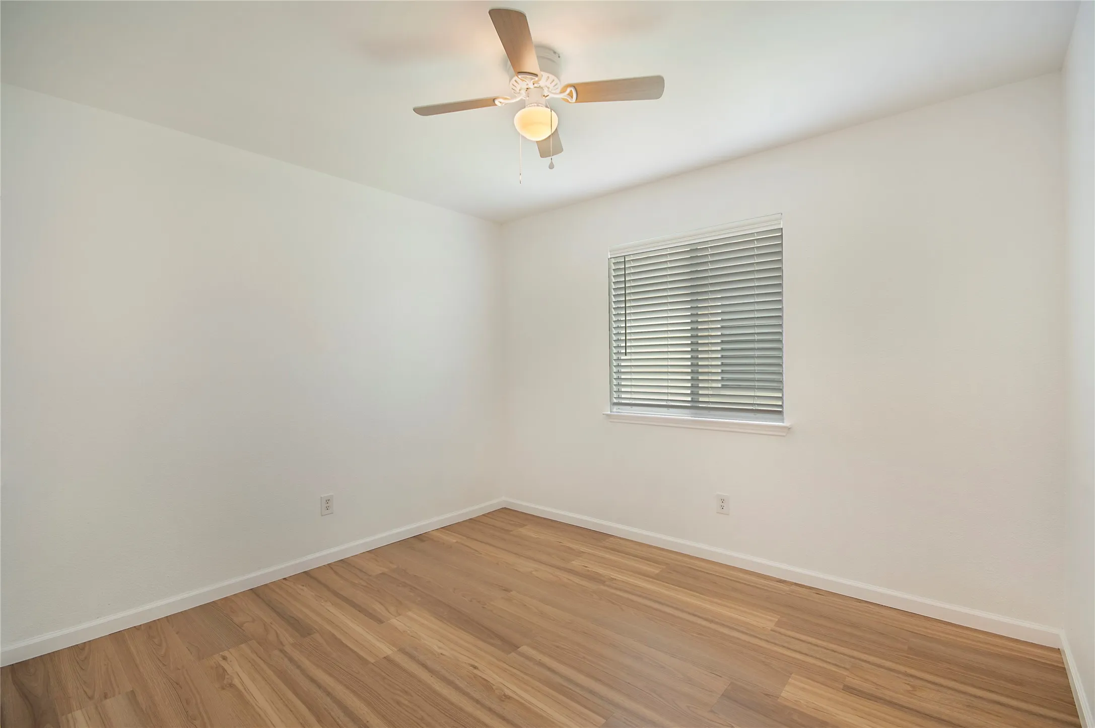Wood-finish flooring, white walls, window with horizontal blinds, and a ceiling fan with integrated lighting