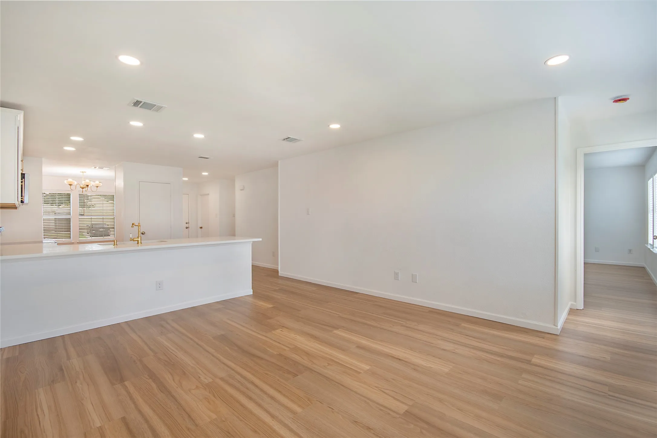 Wood-finish flooring throughout, recessed lighting, and a kitchen featuring white cabinetry, a white countertop, and gold-finish fixtures