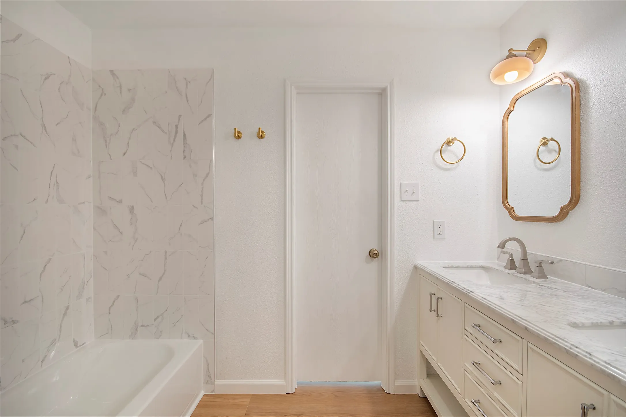 White vanity with double sinks and brushed nickel fixtures, complemented by a decorative mirror and sconce lighting