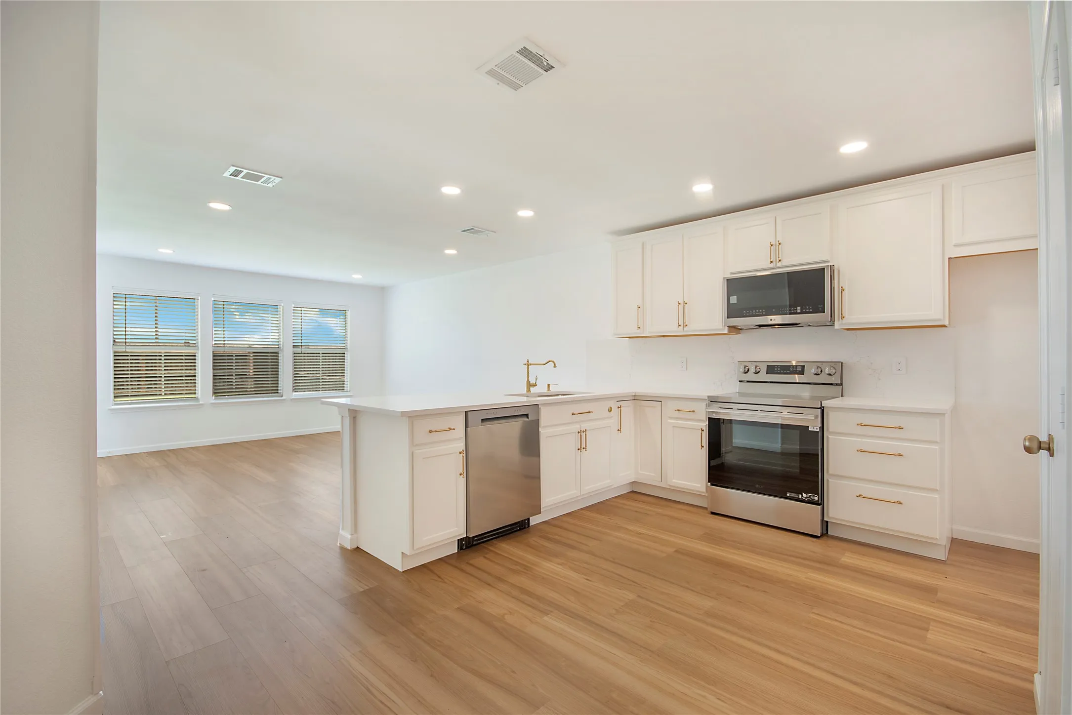 Modern kitchen featuring white cabinetry, stainless steel appliances, light-toned wood-finish flooring, recessed lighting, and a kitchen island with seating