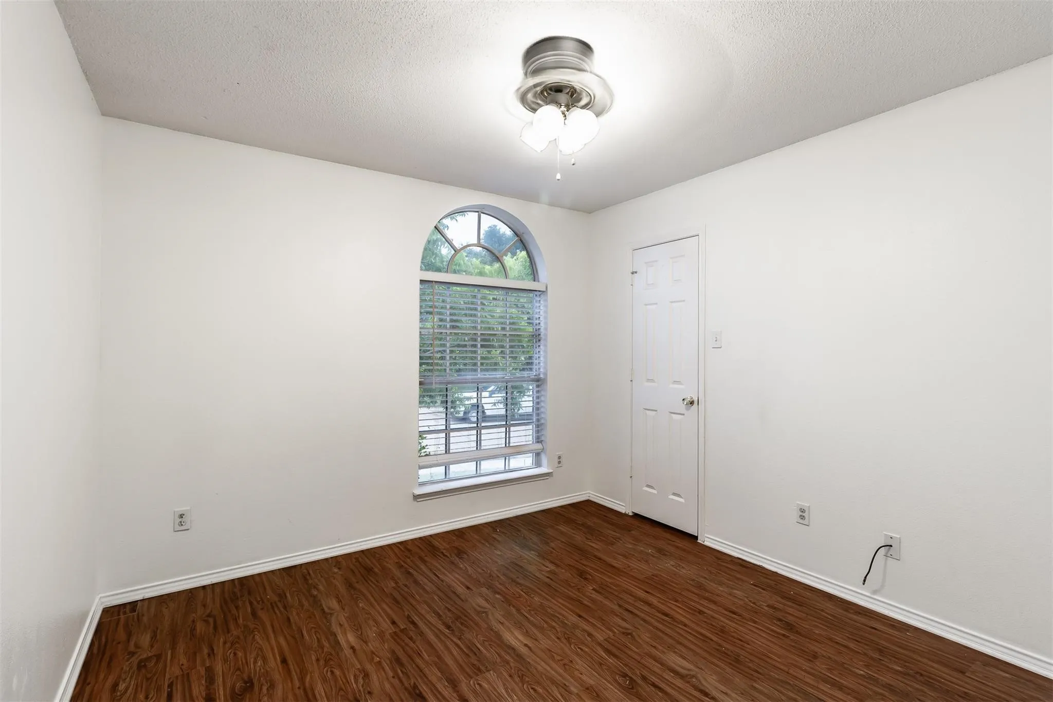 Wood-finish flooring, white walls, and an arched window with blinds
