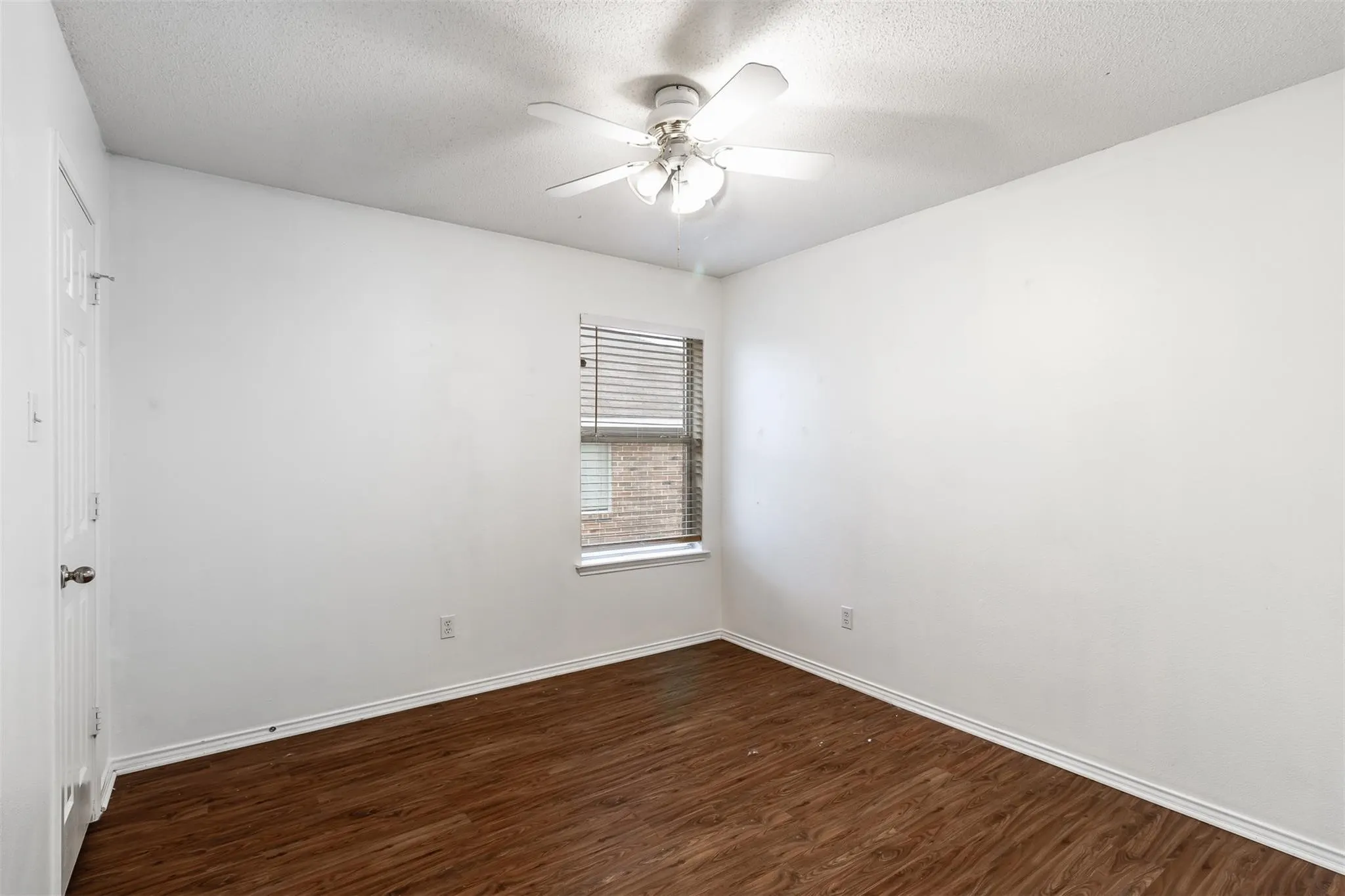 Wood-finish flooring, single window with blinds, ceiling fan with light fixture, and white walls