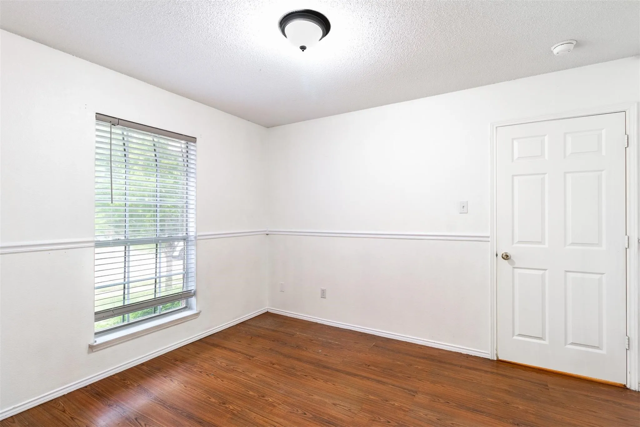 Wood-finish flooring, white paneled door, and window with horizontal blinds