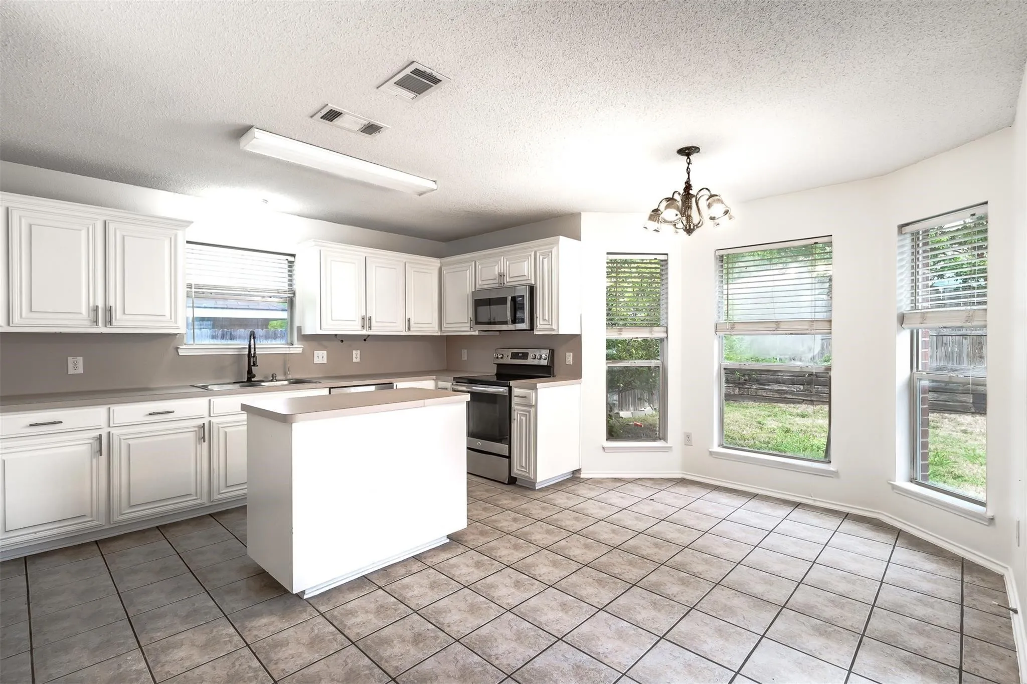 White shaker-style cabinetry, stainless steel appliances, central island, tiled flooring, and multiple windows