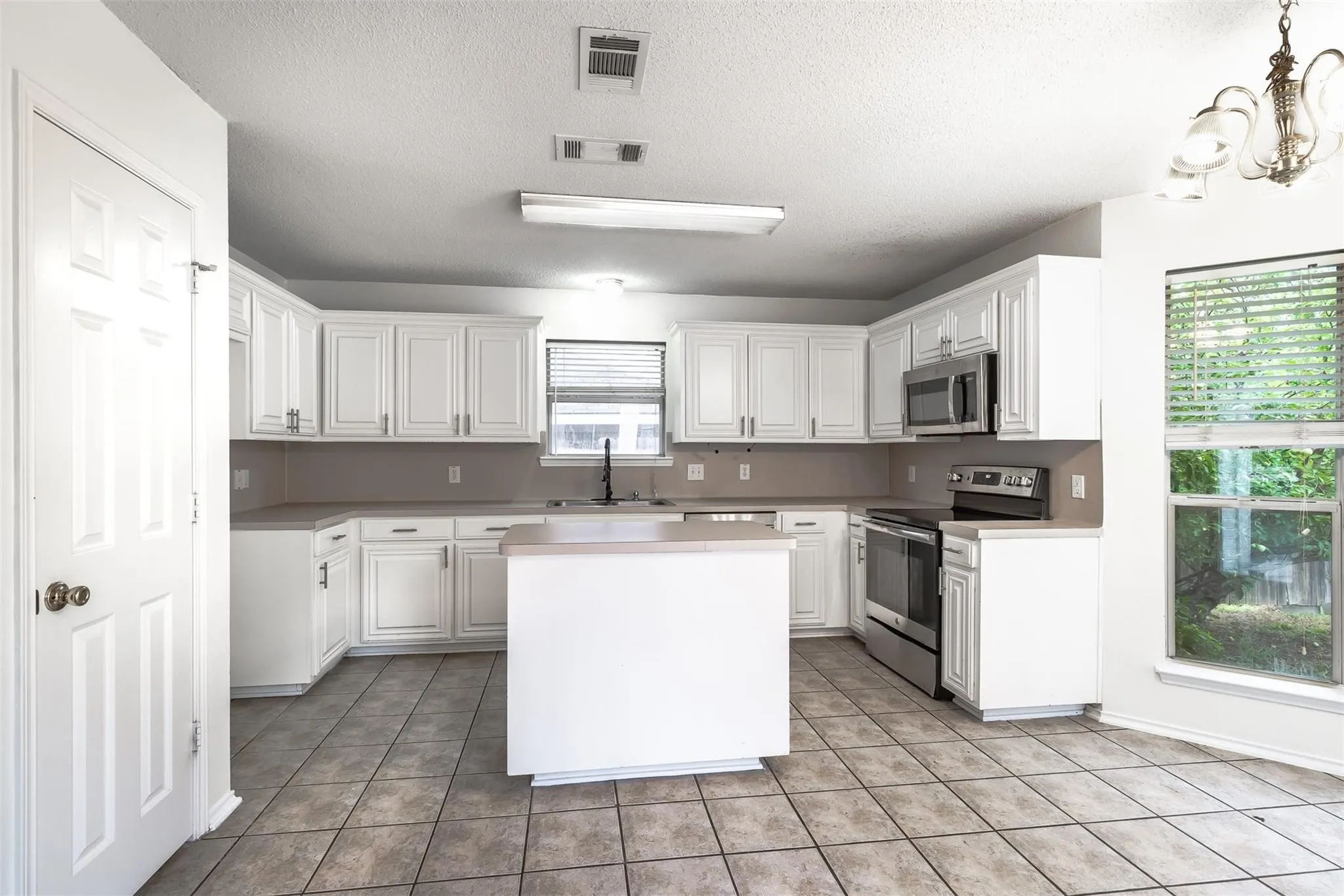 Kitchen featuring white cabinetry, a center island, stainless steel appliances, tile flooring, and a window with blinds