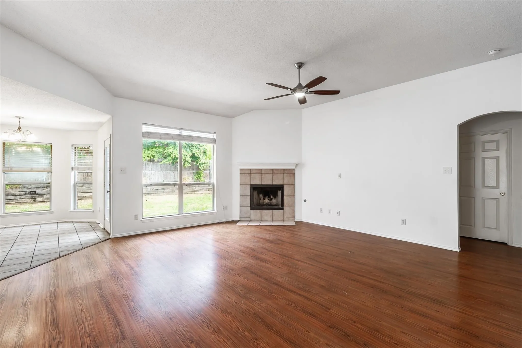 Wood-finish flooring throughout the main living space, a tiled fireplace with hearth, a ceiling fan, and large windows with outdoor views