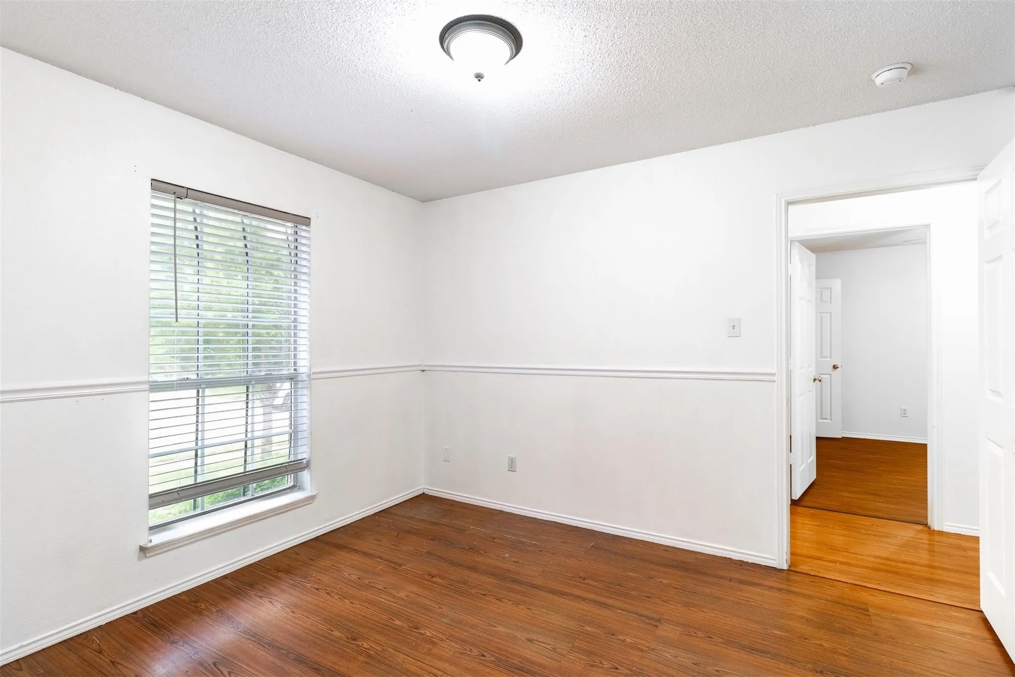 Wood-finish flooring, white walls with chair rail molding, and a single window with blinds