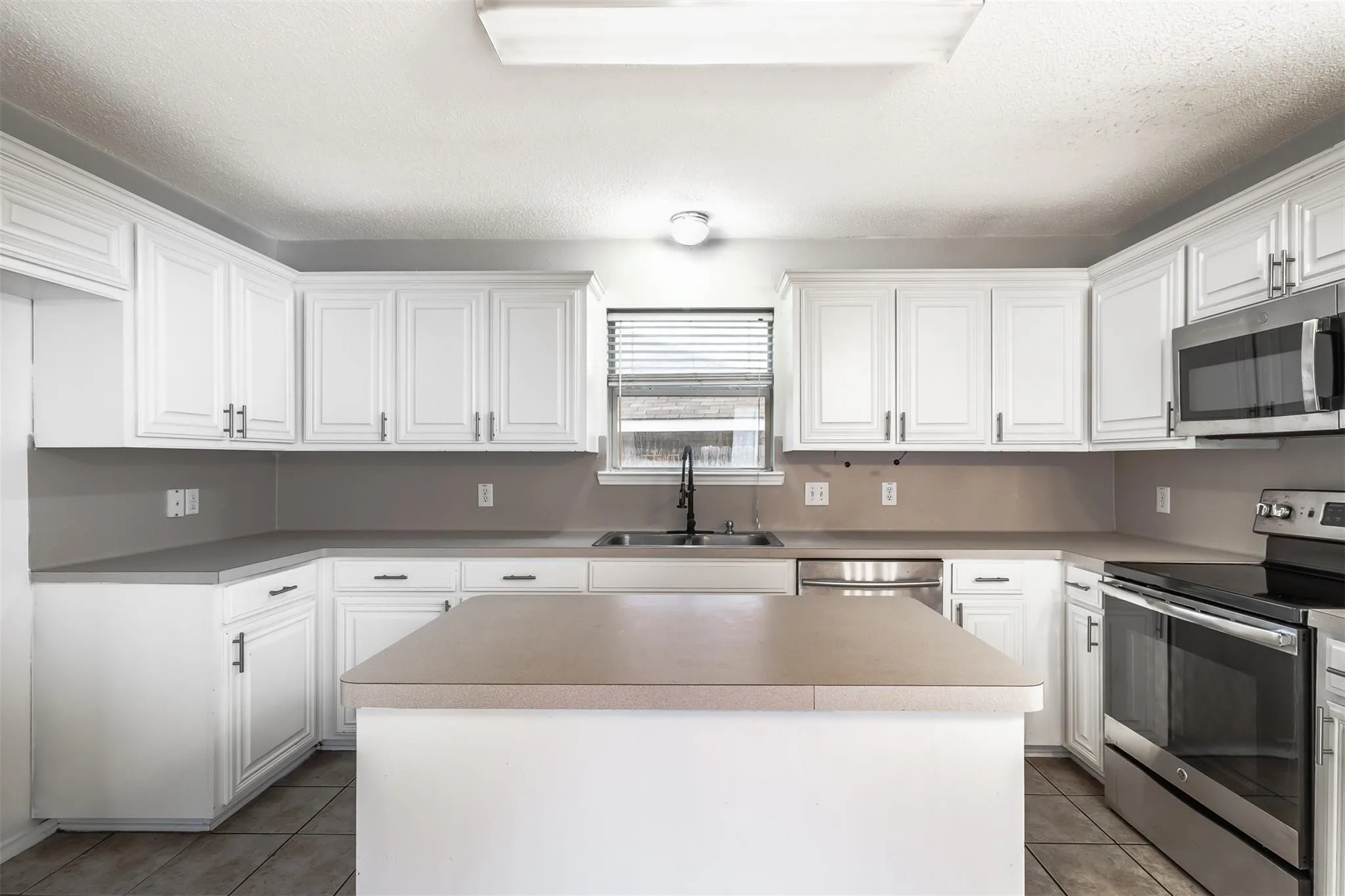 White cabinetry, gray countertops, stainless steel appliances, central island, and tiled flooring