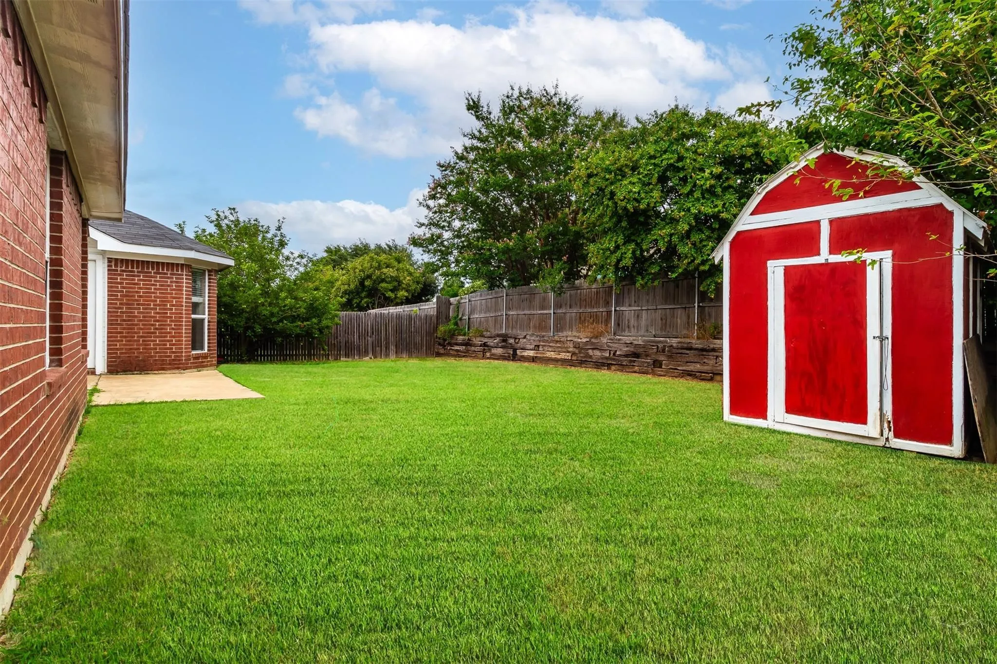 Expansive green lawn, red barn-style shed, private wood fence, brick exterior with white trim, and a concrete patio