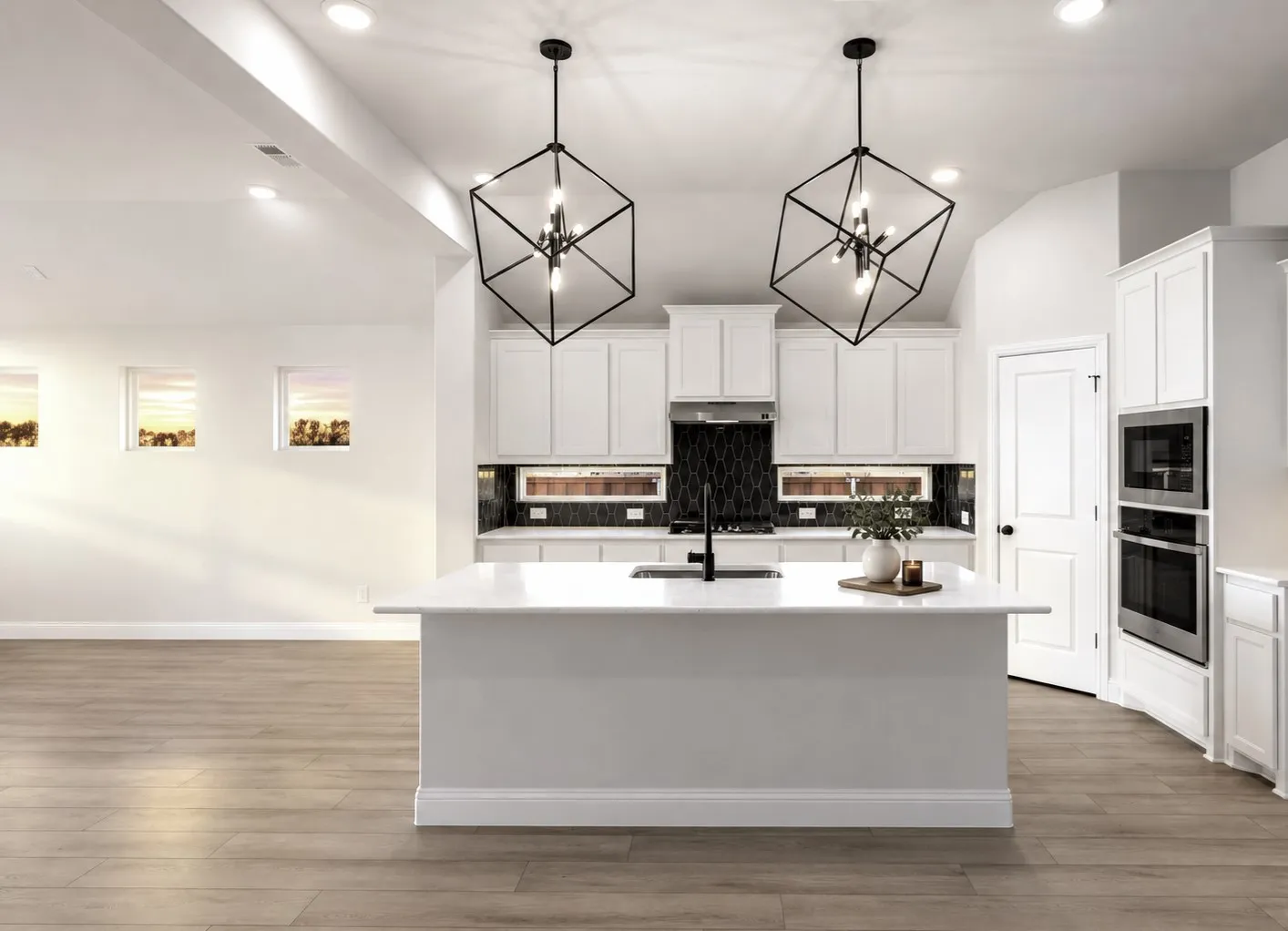 Open-concept kitchen featuring an island with a light-toned countertop, white cabinetry, integrated stainless steel appliances, and wood-finish flooring