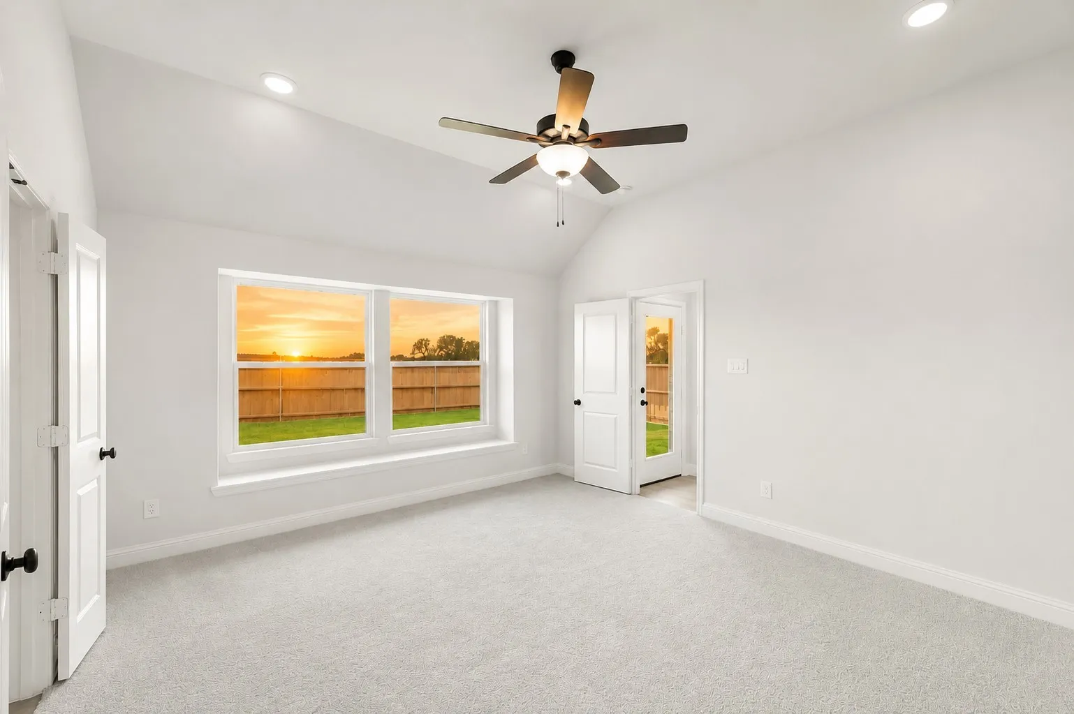 Vaulted ceiling, recessed lighting, ceiling fan with light fixture, light gray carpeting, and a window with a wooden fence background