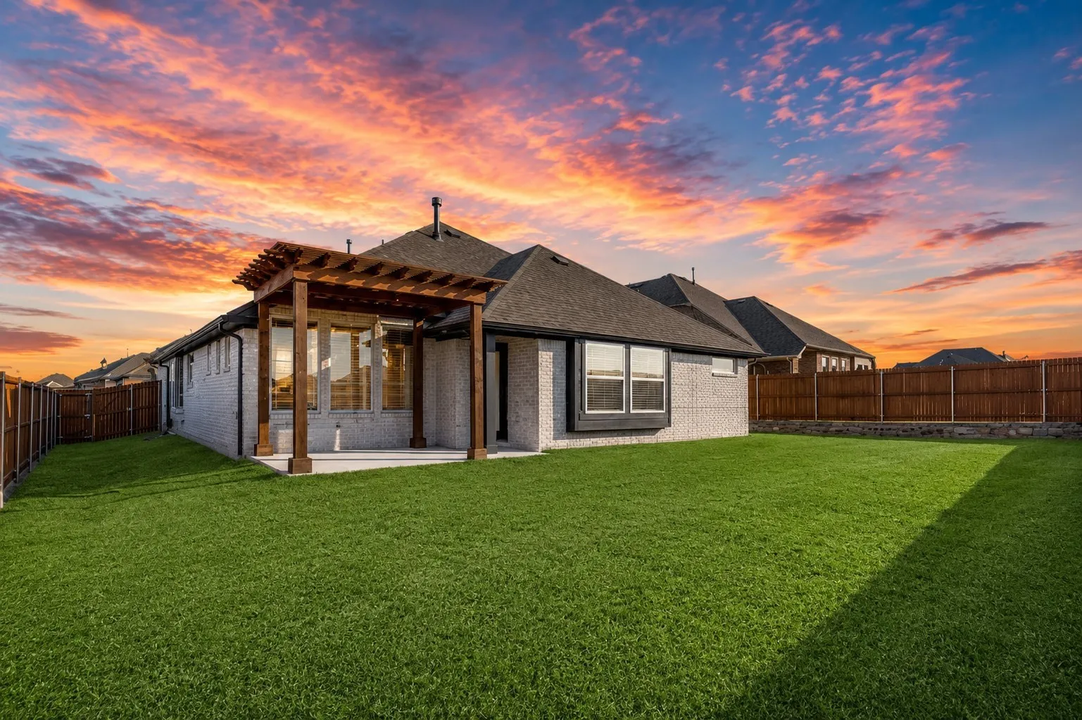 Expansive backyard featuring a manicured lawn, a large concrete patio, and a wood pergola