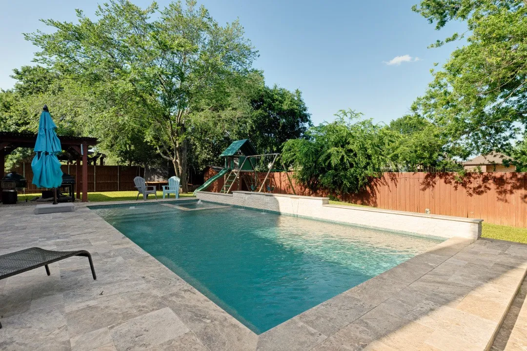 Resort-style backyard featuring a heated pool and spa with tranquil water features, surrounded by elegant travertine decking.