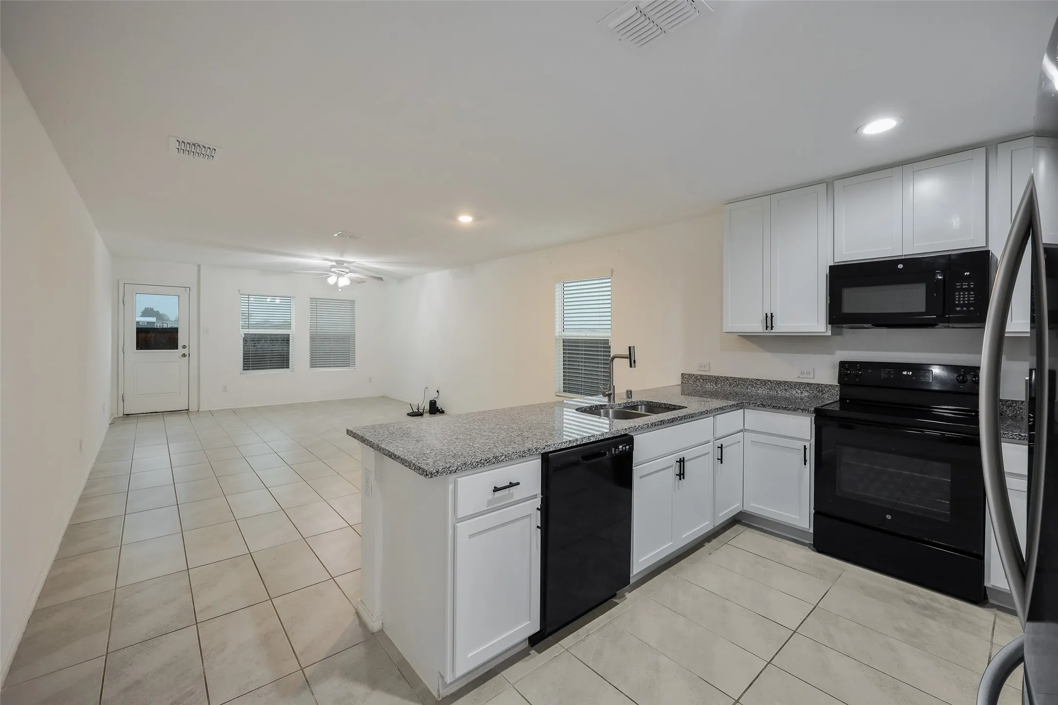 Open-concept kitchen with white cabinetry, granite-style countertops, stainless-steel sink, and black appliances