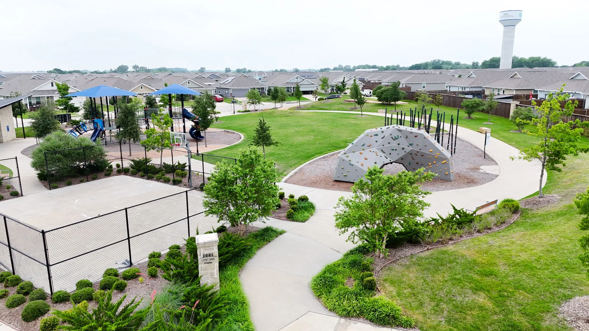 Expansive green space featuring recreational courts, a children's play area with shaded structures, and a rock climbing feature