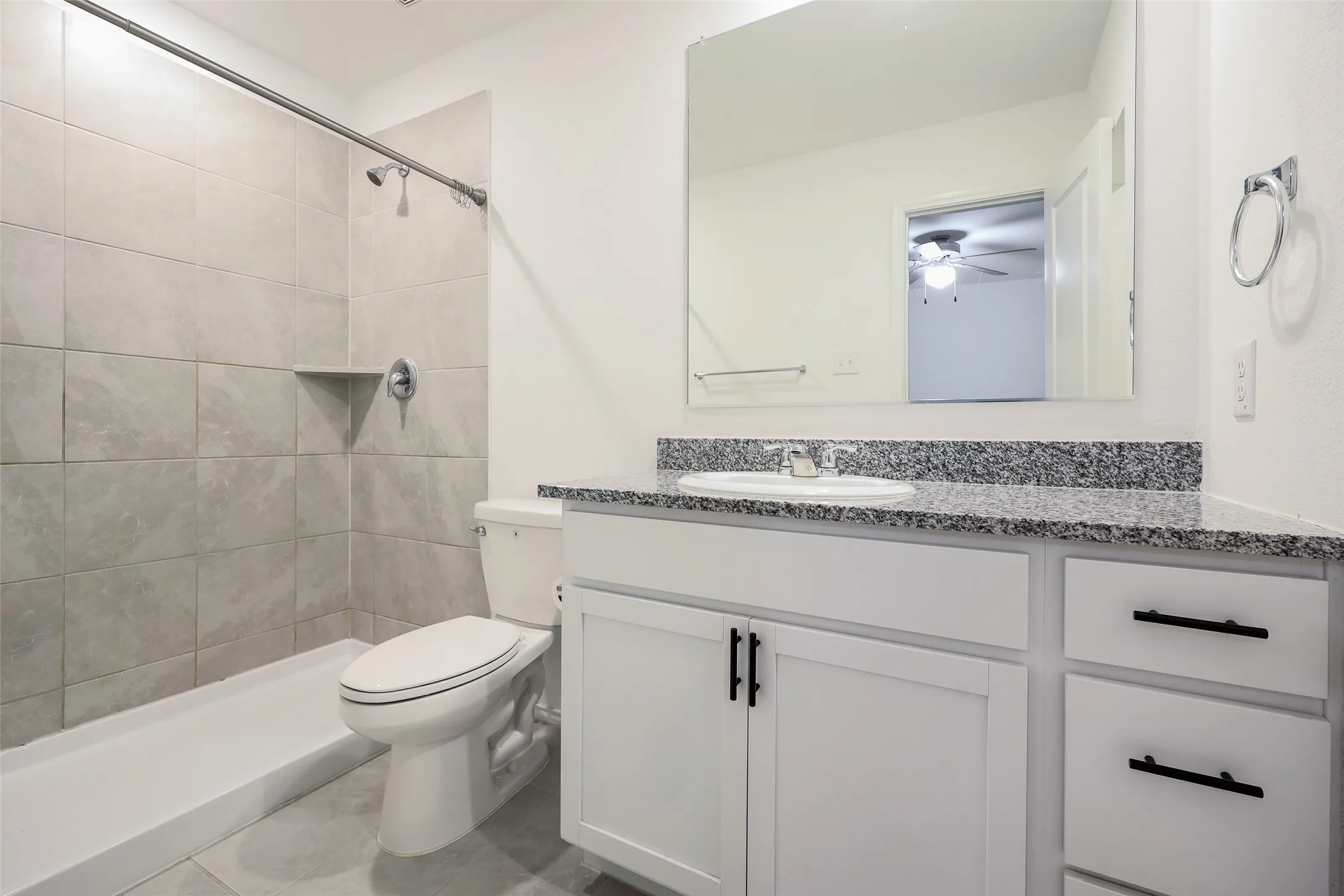 Bathroom featuring a tiled shower surround, built-in shower shelf, contemporary vanity with a granite-style countertop, and a large wall-mounted mirror