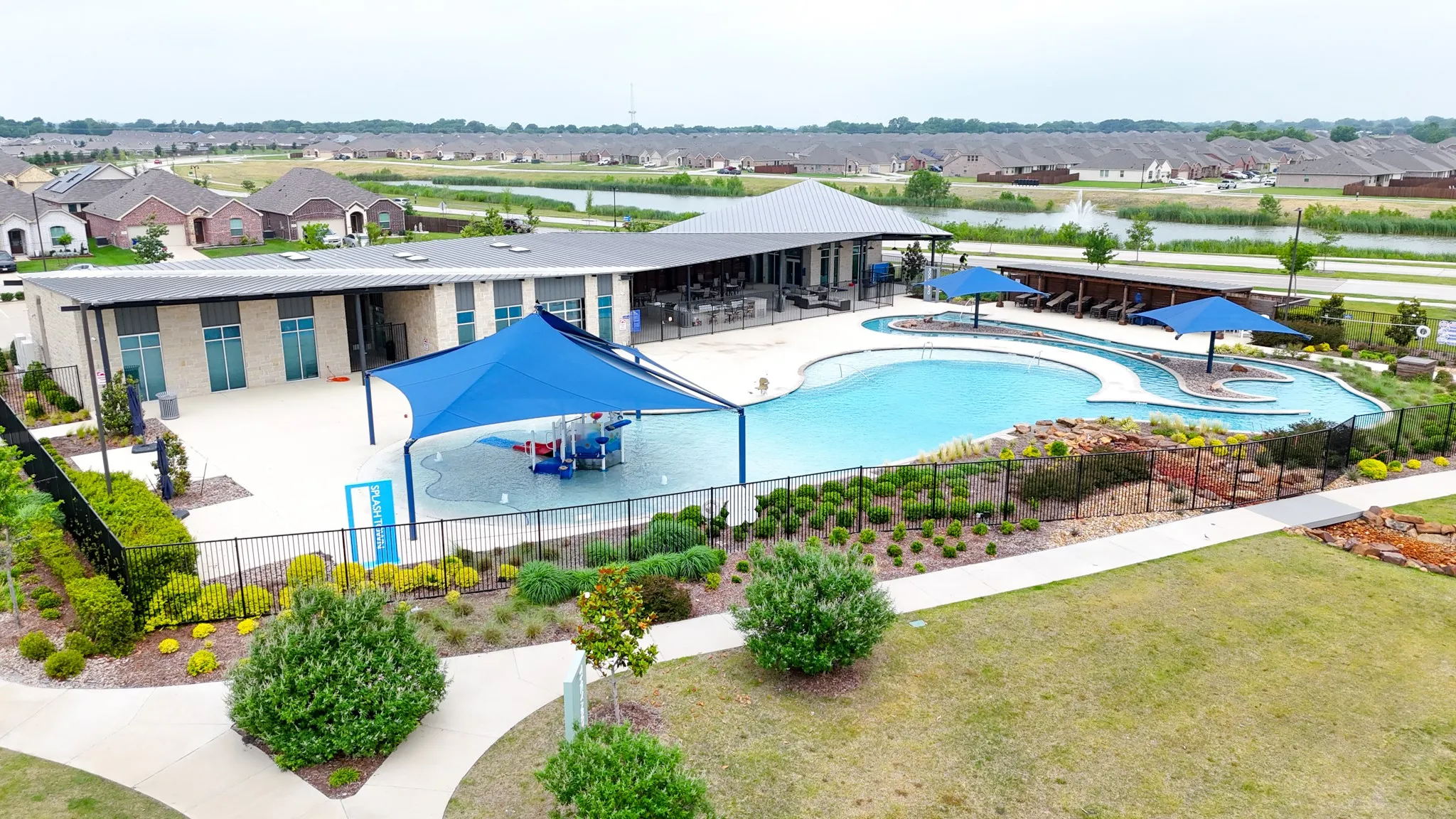 Community amenity center featuring a swimming pool, shaded splash pad, and a separate flowing water feature