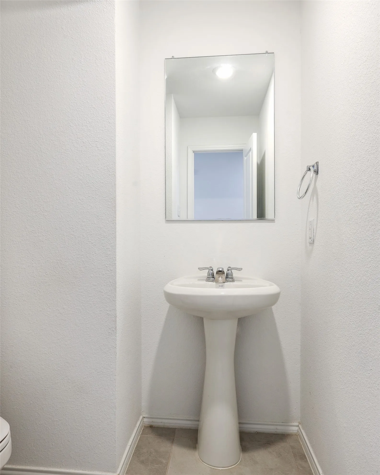Pedestal sink with chrome faucet, rectangular mirror, and light-toned flooring