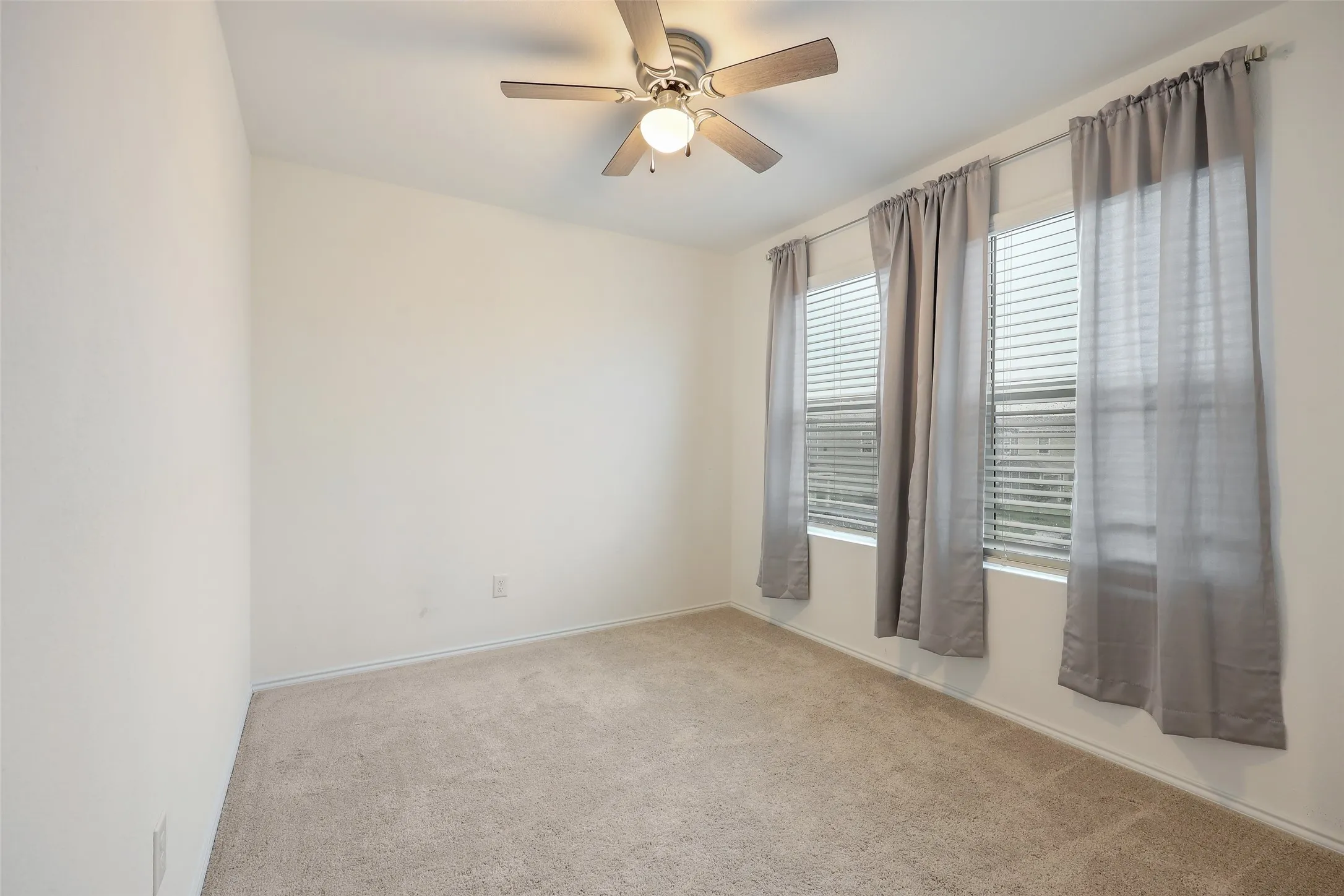 Neutral wall tones, ceiling fan with integrated lighting, two windows with blinds, and carpeting