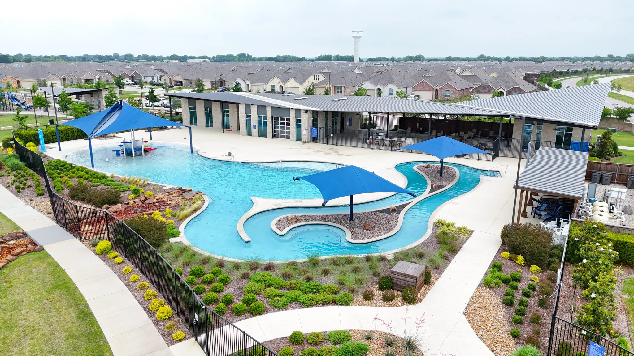 Community swimming pool with a distinct lazy river, adjacent to a contemporary recreation building featuring a covered patio