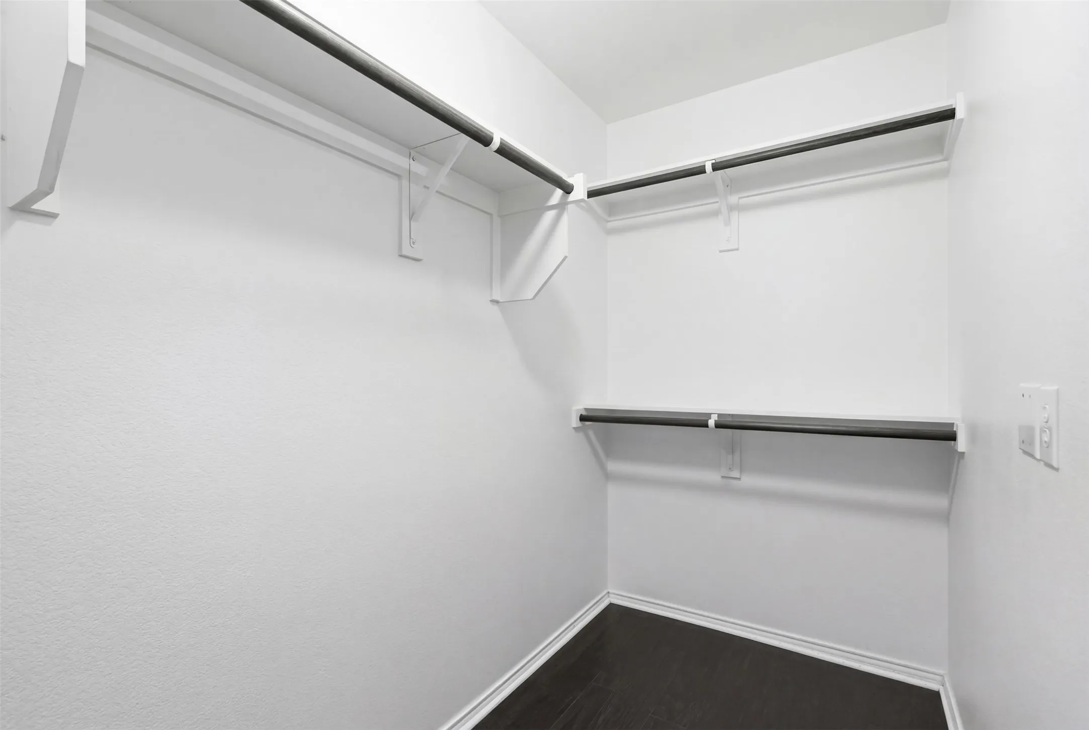 Walk-in closet featuring built-in shelving, hanging rods, and dark wood-finish flooring