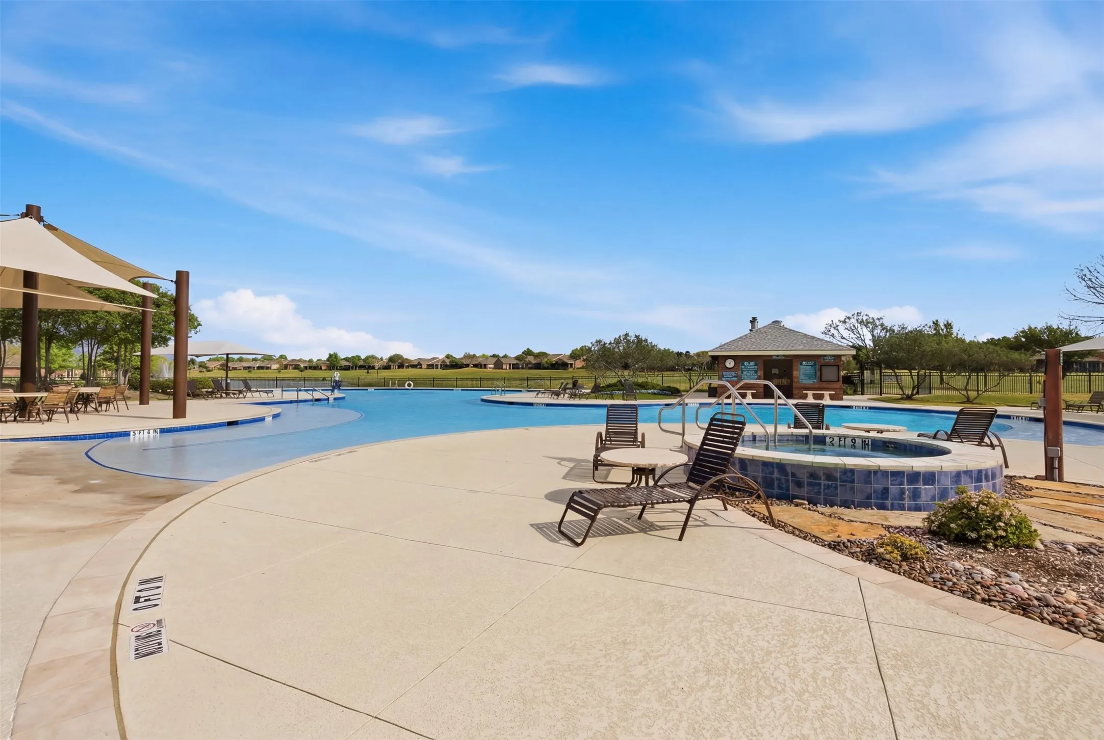 Expansive community pool with an integrated spa, surrounding concrete decking, and shaded seating areas