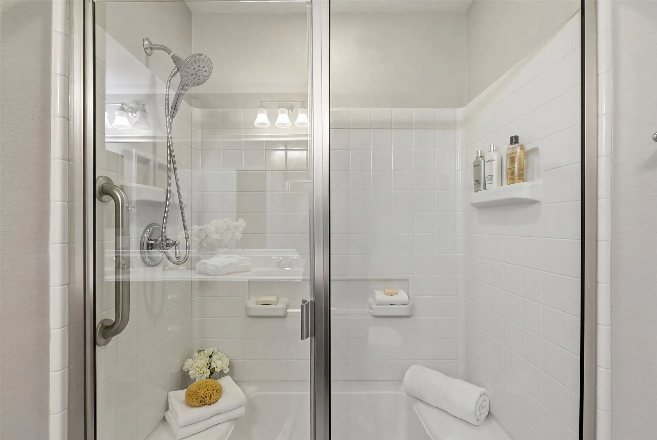 Glass-enclosed shower with white tiled walls, a built-in bench, and a brushed nickel grab bar