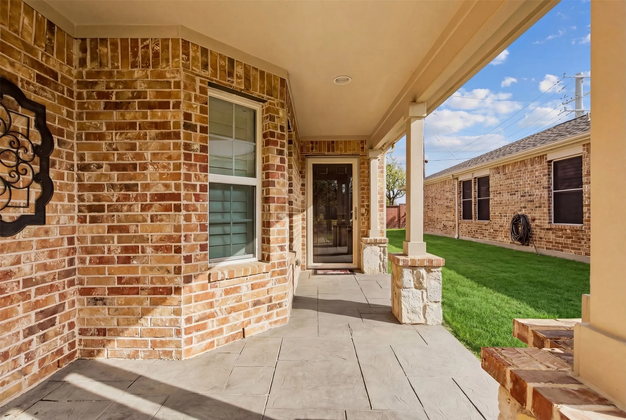 Brick exterior with stone accents, covered entry, stamped concrete patio, and a storm door