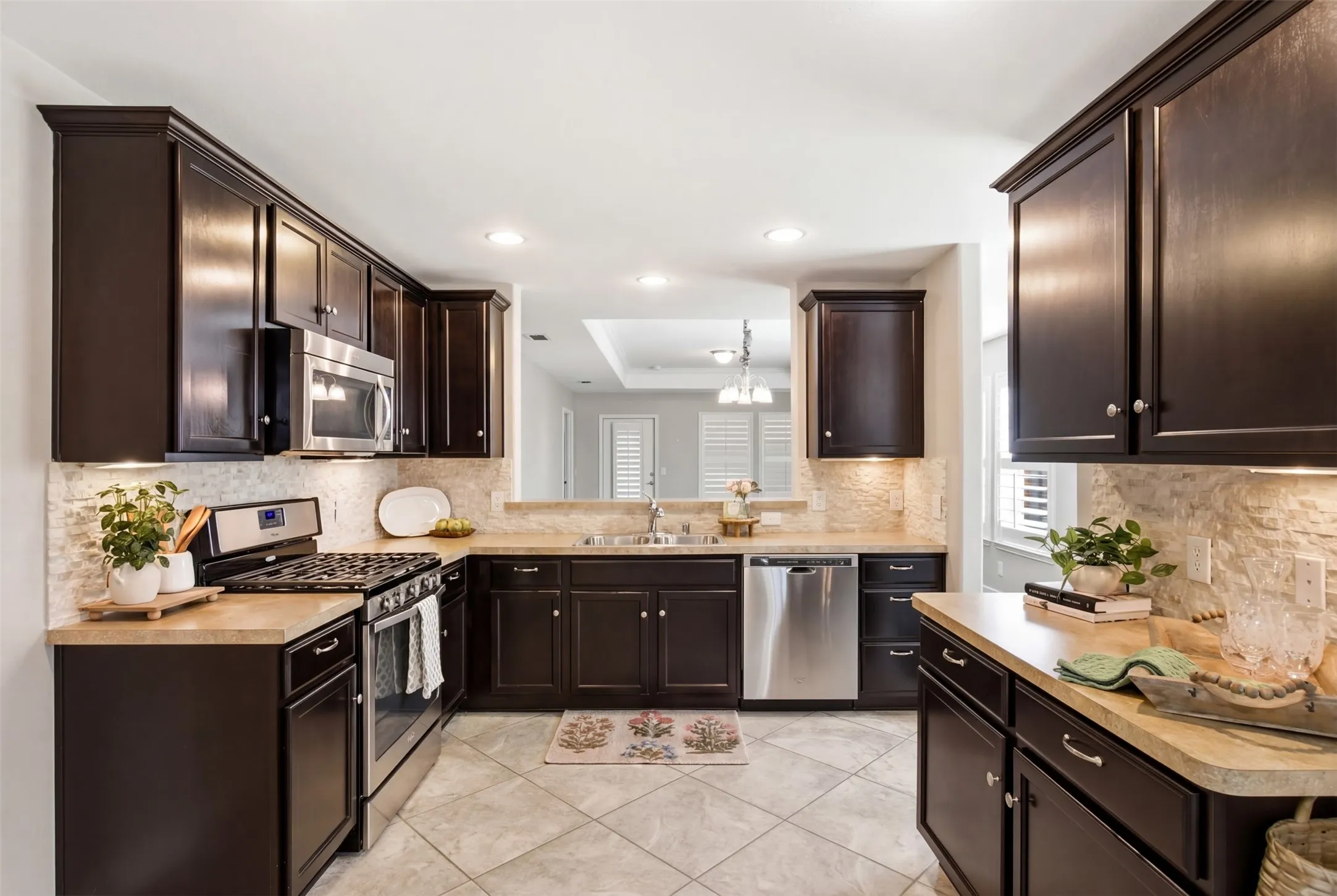 Kitchen featuring dark wood cabinetry, stainless steel appliances, a stone-finish backsplash, light-toned countertops, and recessed lighting