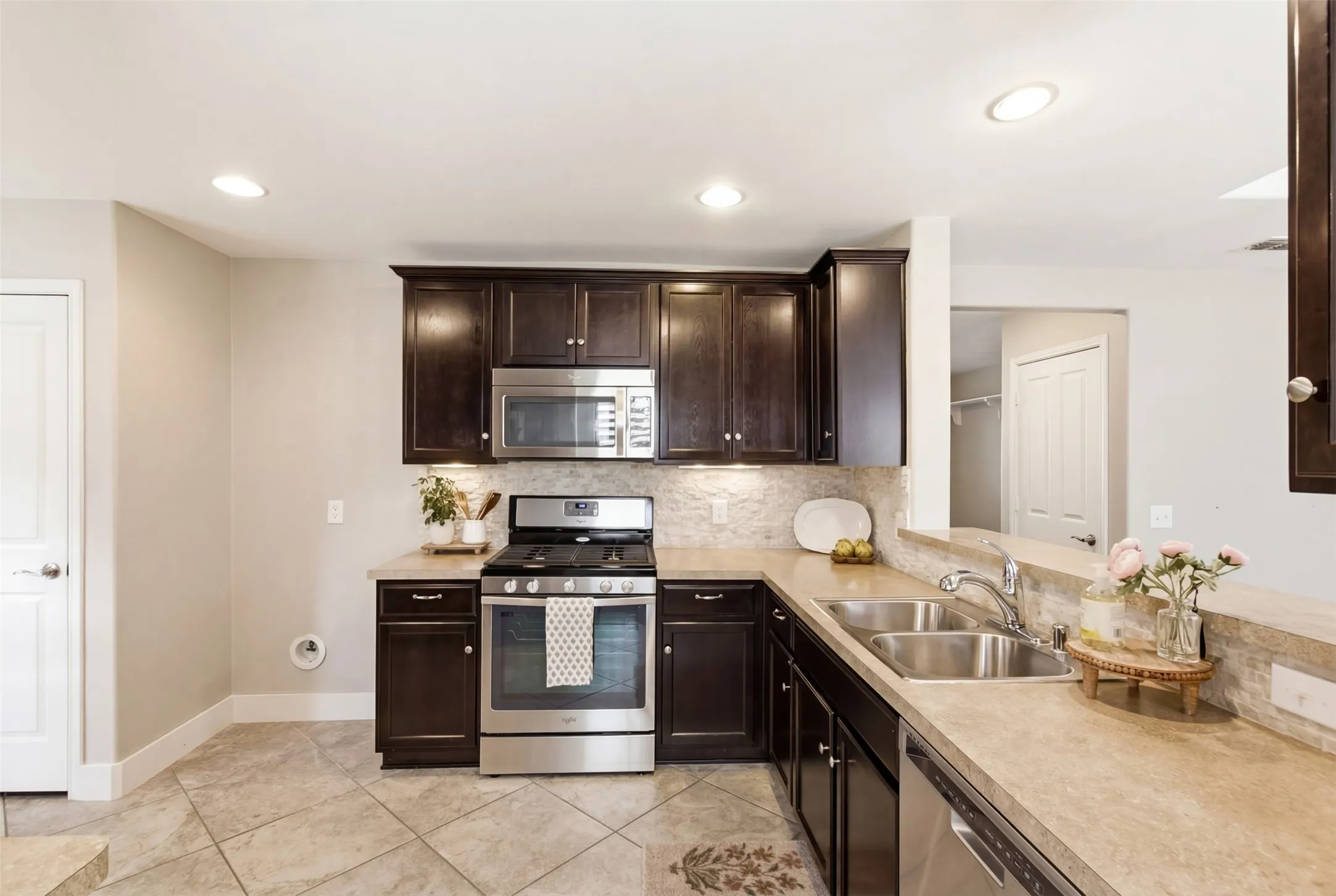 Dark wood-finish cabinetry with stainless steel appliances, dual basin sink, and recessed lighting
