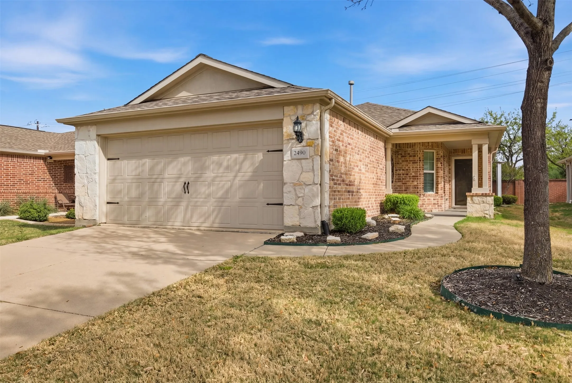 Brick and stone exterior with a covered entry, attached garage, concrete driveway, and established landscaping