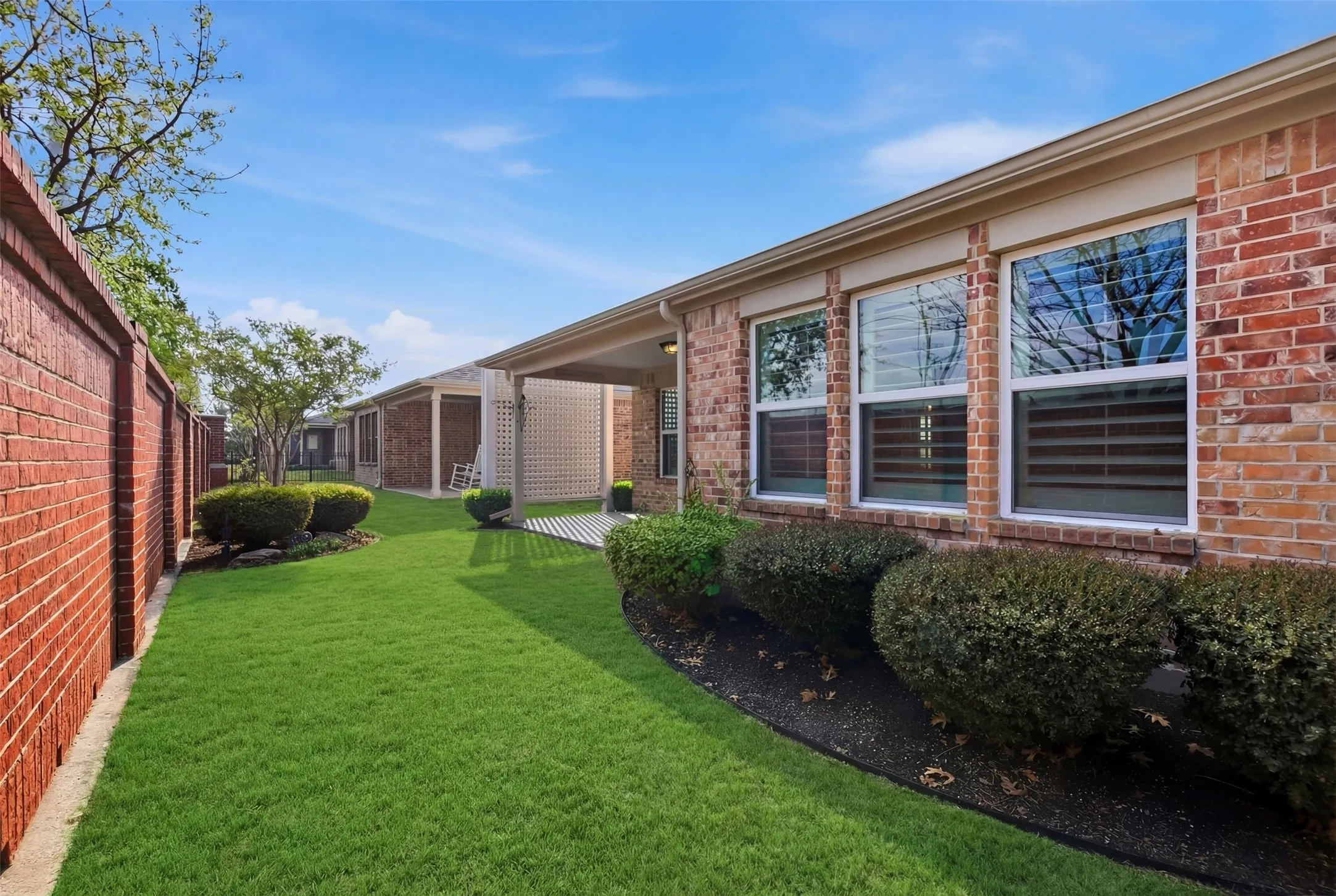 Brick exterior with white-framed windows, a covered patio, and manicured landscaping