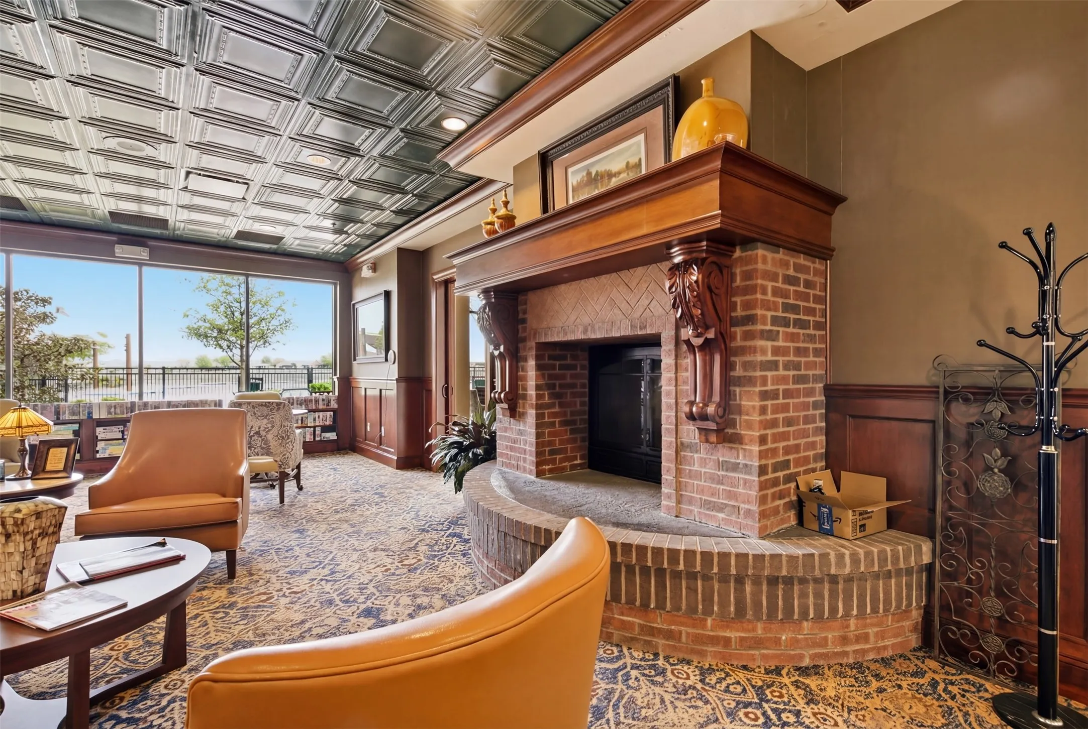 Brick fireplace with a wood-finish mantel and corbel accents, tin-panel ceiling, full-light windows, and wood-panel wainscoting