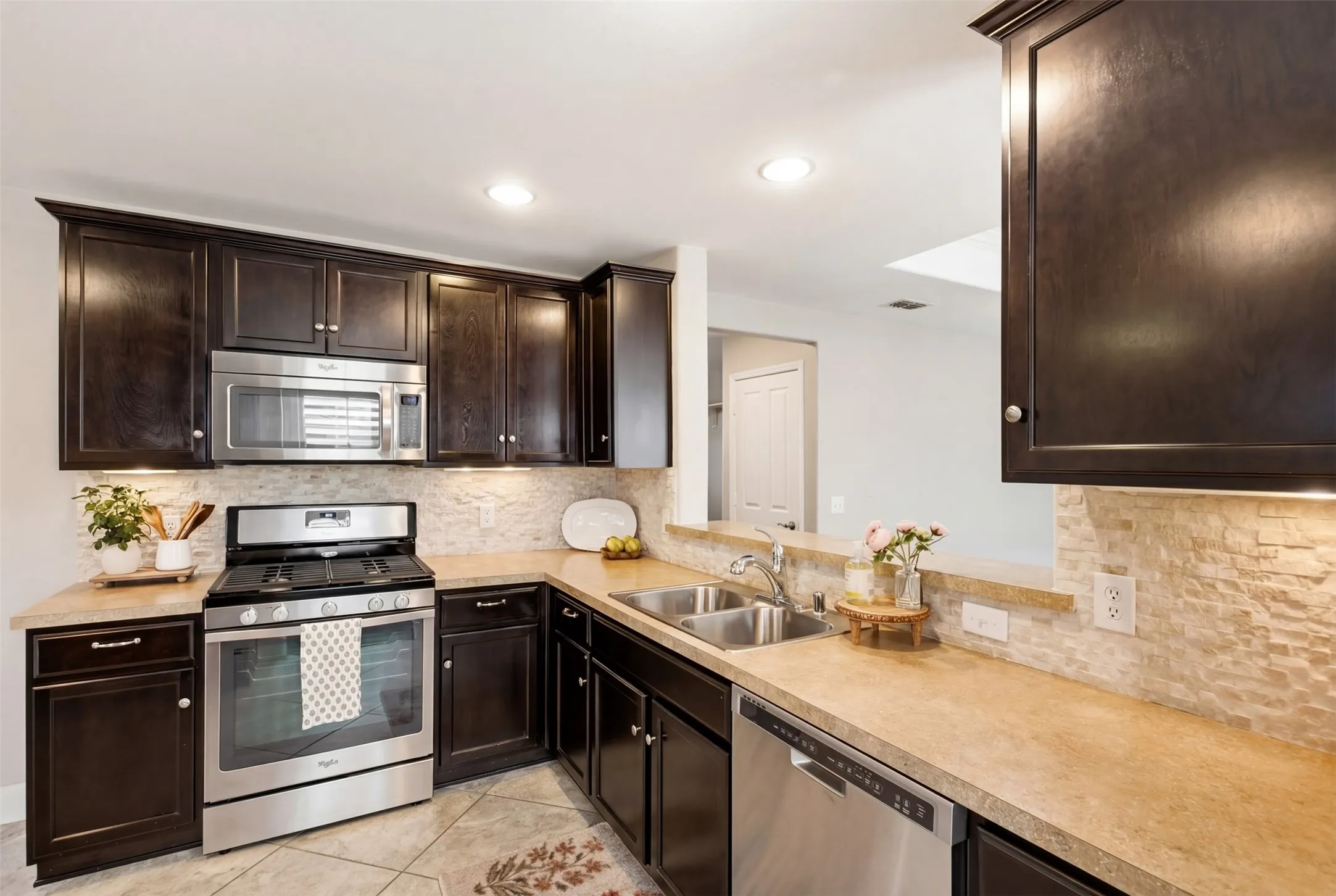 Kitchen featuring dark wood cabinetry, stainless steel appliances, stone tile backsplash, and light-toned countertops