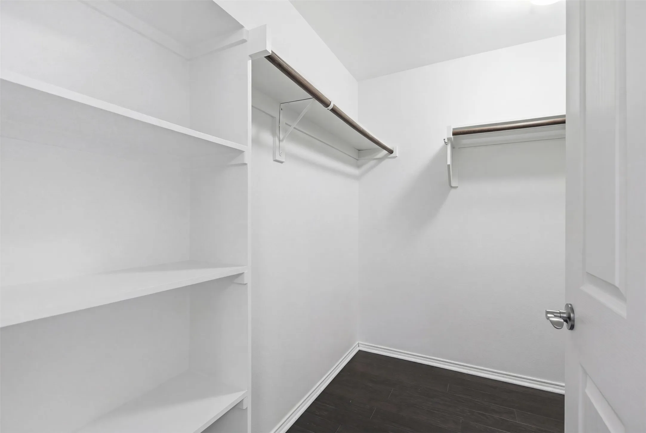 Spacious closet featuring dark wood-finish flooring, built-in shelving, and multiple clothing rods
