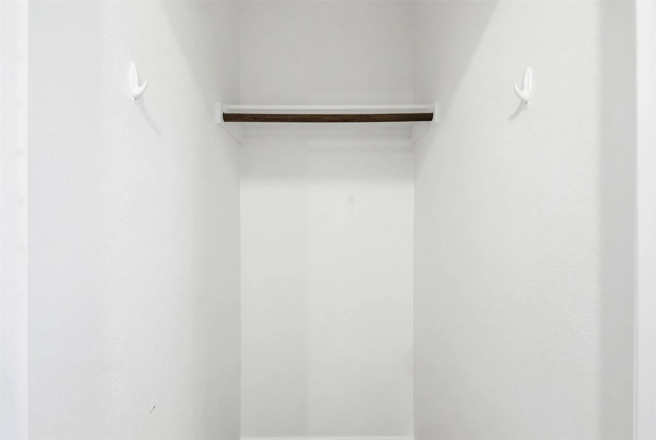 Built-in closet system featuring a wooden hanging rod, white shelf, and two wall-mounted hooks