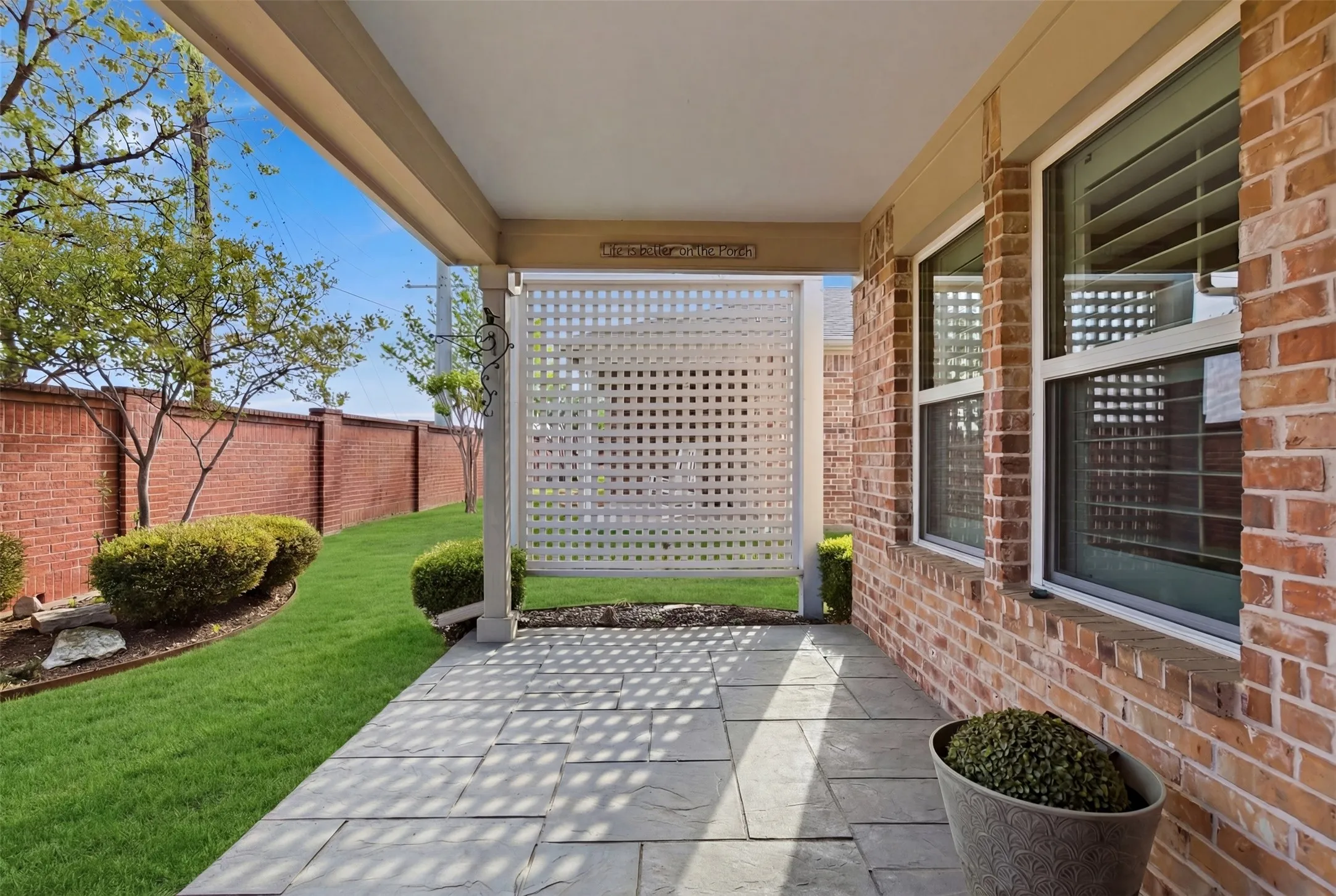 Covered patio featuring stone pavers, a white lattice privacy screen, and a surrounding brick wall