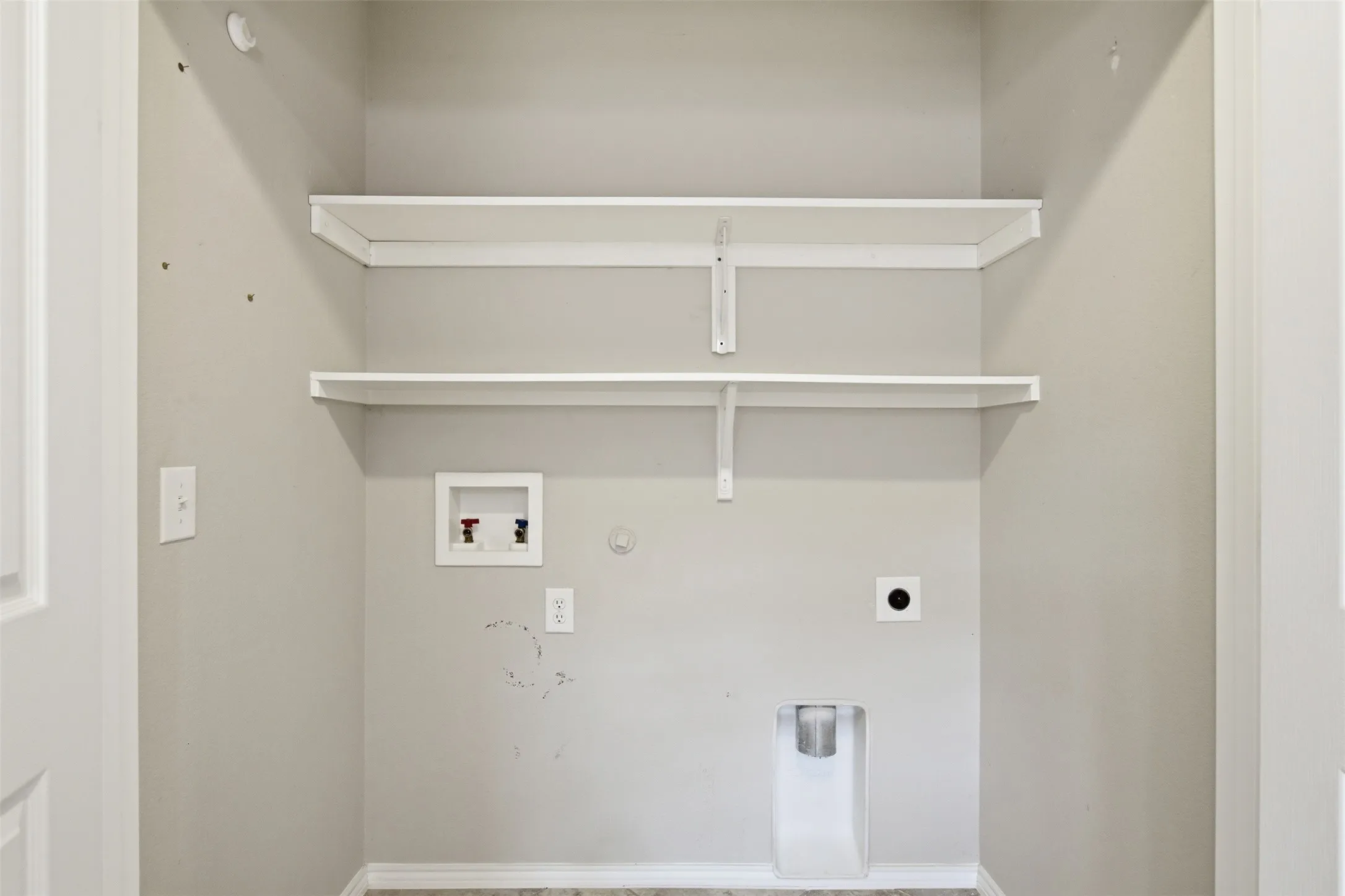 Dedicated laundry area featuring a utility sink connection, washer/dryer hookups, and two built-in storage shelves