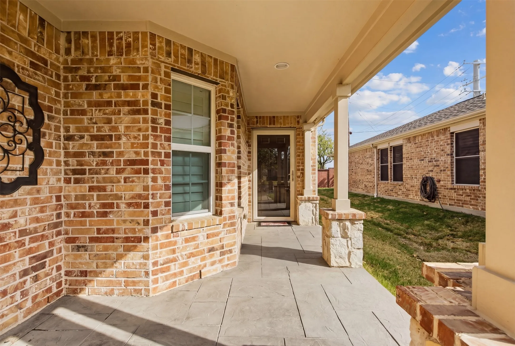 Brick exterior facade, covered porch with stone-wrapped columns, stamped concrete flooring, and an entry door with glass insert